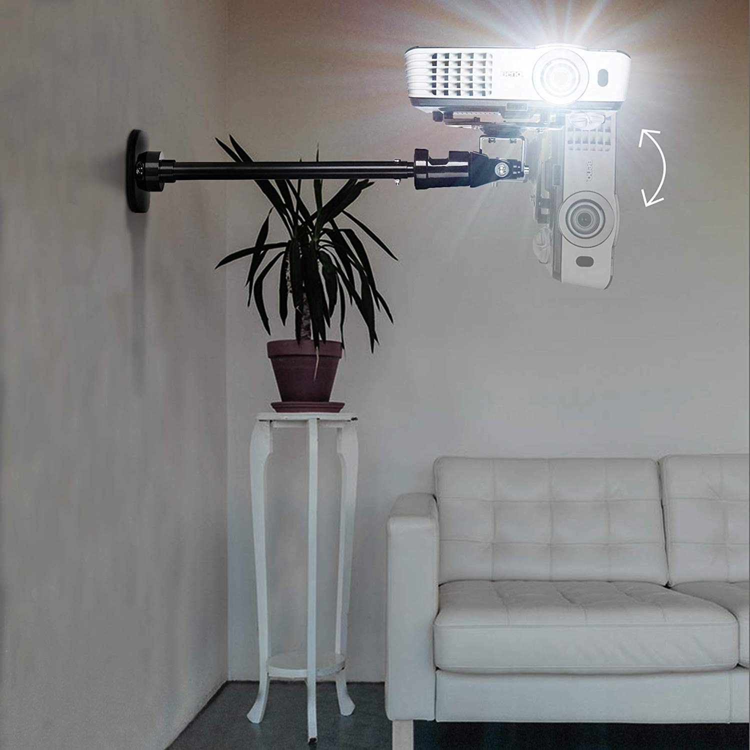 Proyector montado en un brazo de pared, una planta en un soporte y un sofá blanco.
