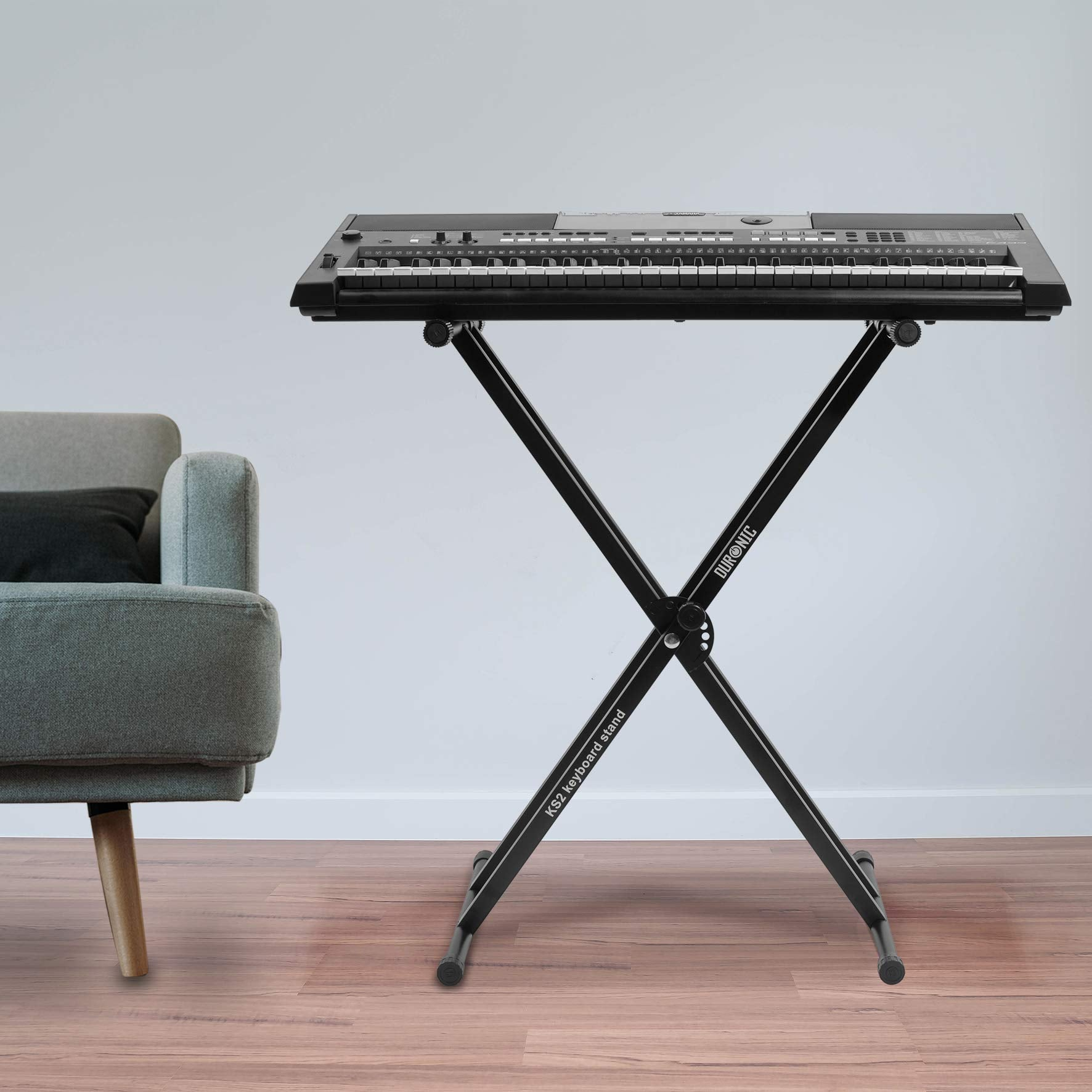 Teclado negro sobre un soporte, en una habitación. Sofá gris en el fondo.