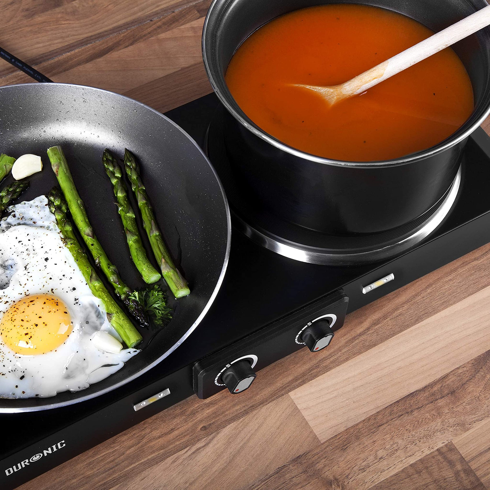 Kochszene: Pfanne mit Ei und Spargel, Topf mit Suppe auf dem Herd.