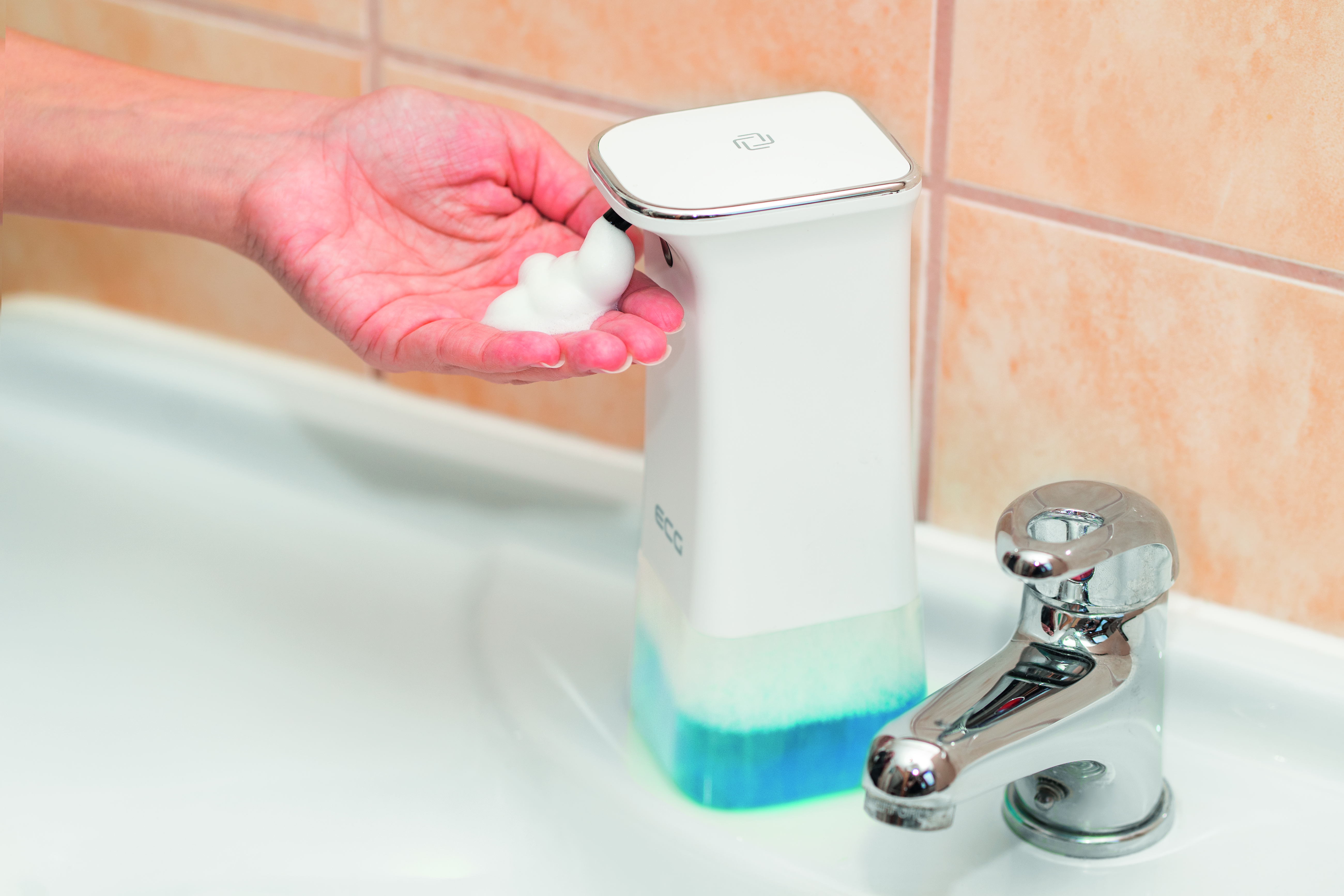 Eine Hand, die Schaumseife abgibt. Der Seifenspender ist weiß und blau. Im Hintergrund ist ein verchromter Wasserhahn.