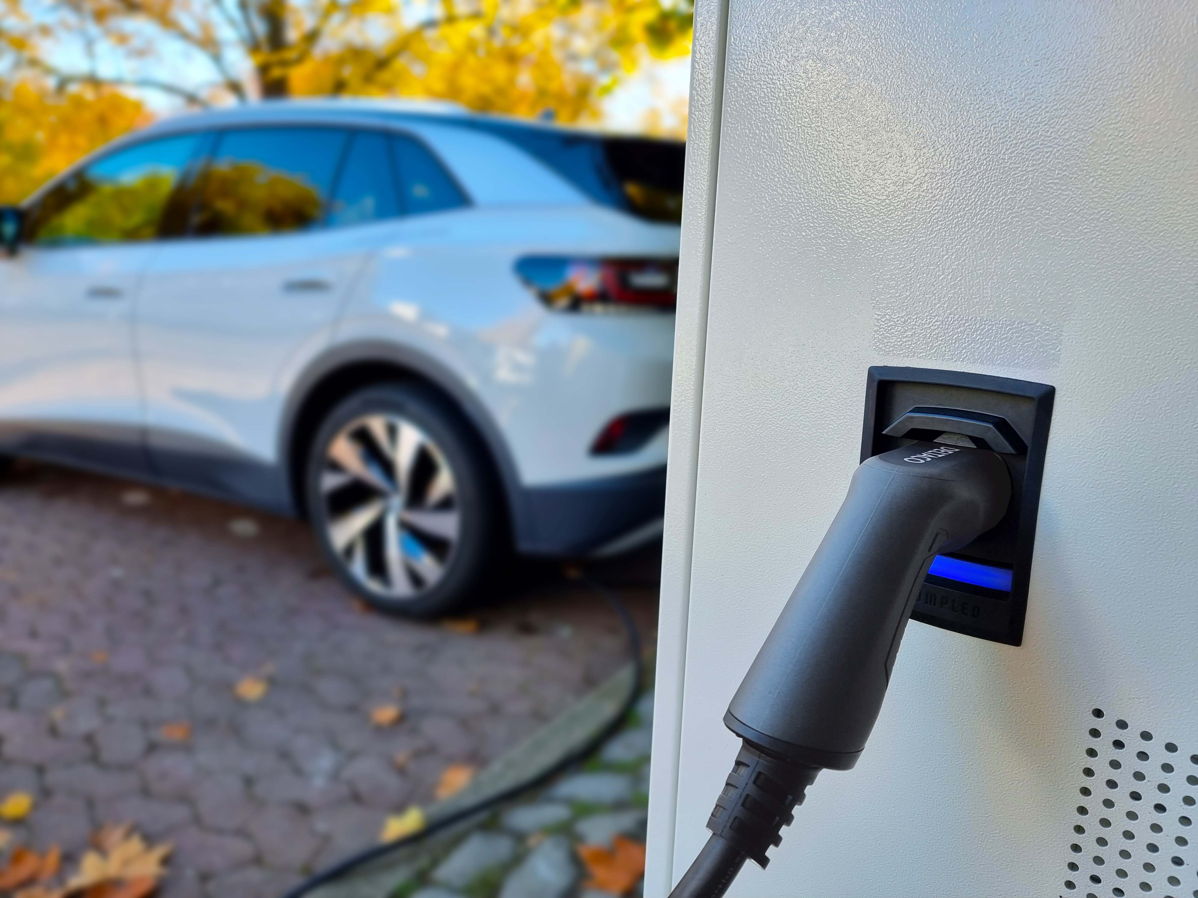 An electric car charging. The charger is plugged in. Blurred background with trees.