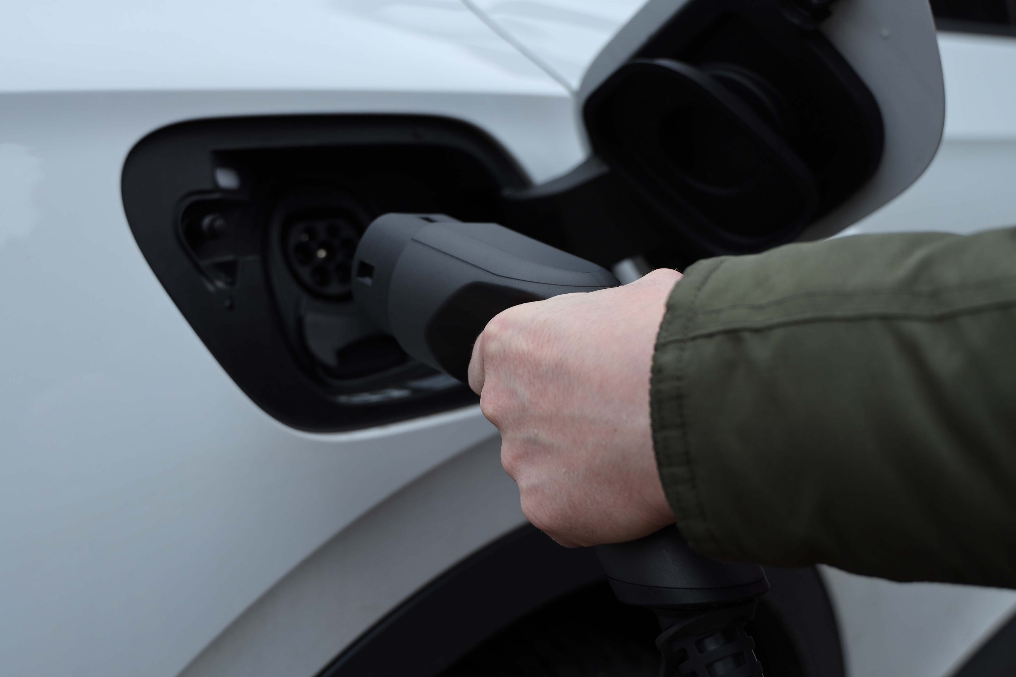 Eine Hand steckt ein Ladekabel in ein weißes Elektroauto.
