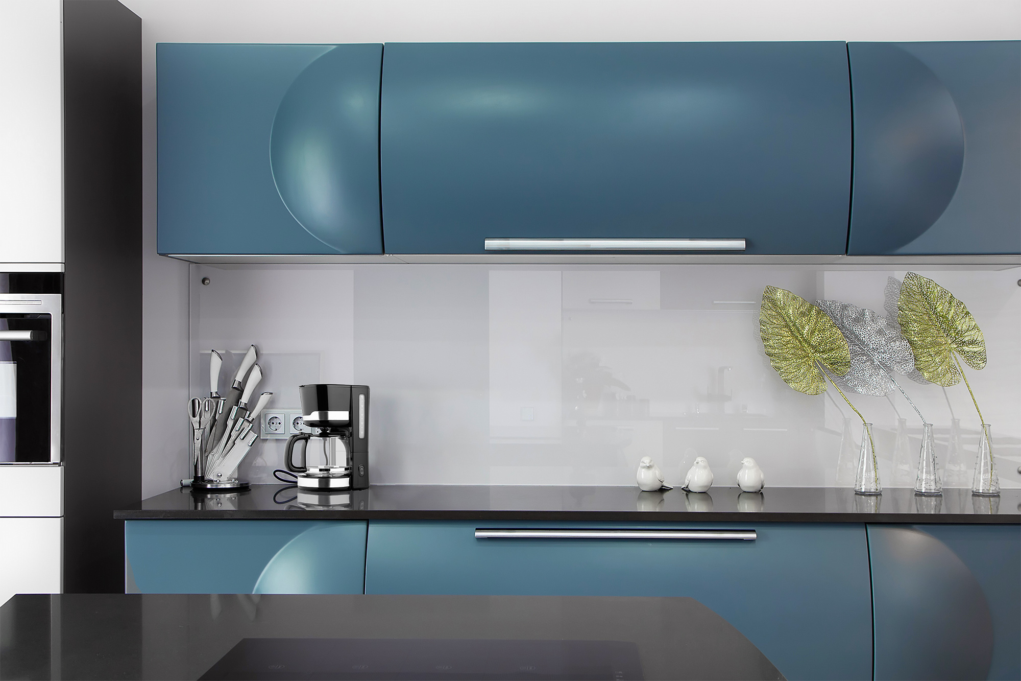 Cocina moderna con gabinetes azules, salpicadero blanco y encimera negra con electrodomésticos.
