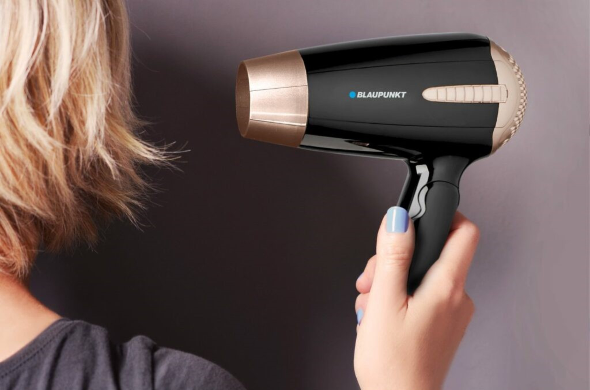 Mujer sosteniendo un secador de pelo negro y dorado. La marca Blaupunkt es visible.