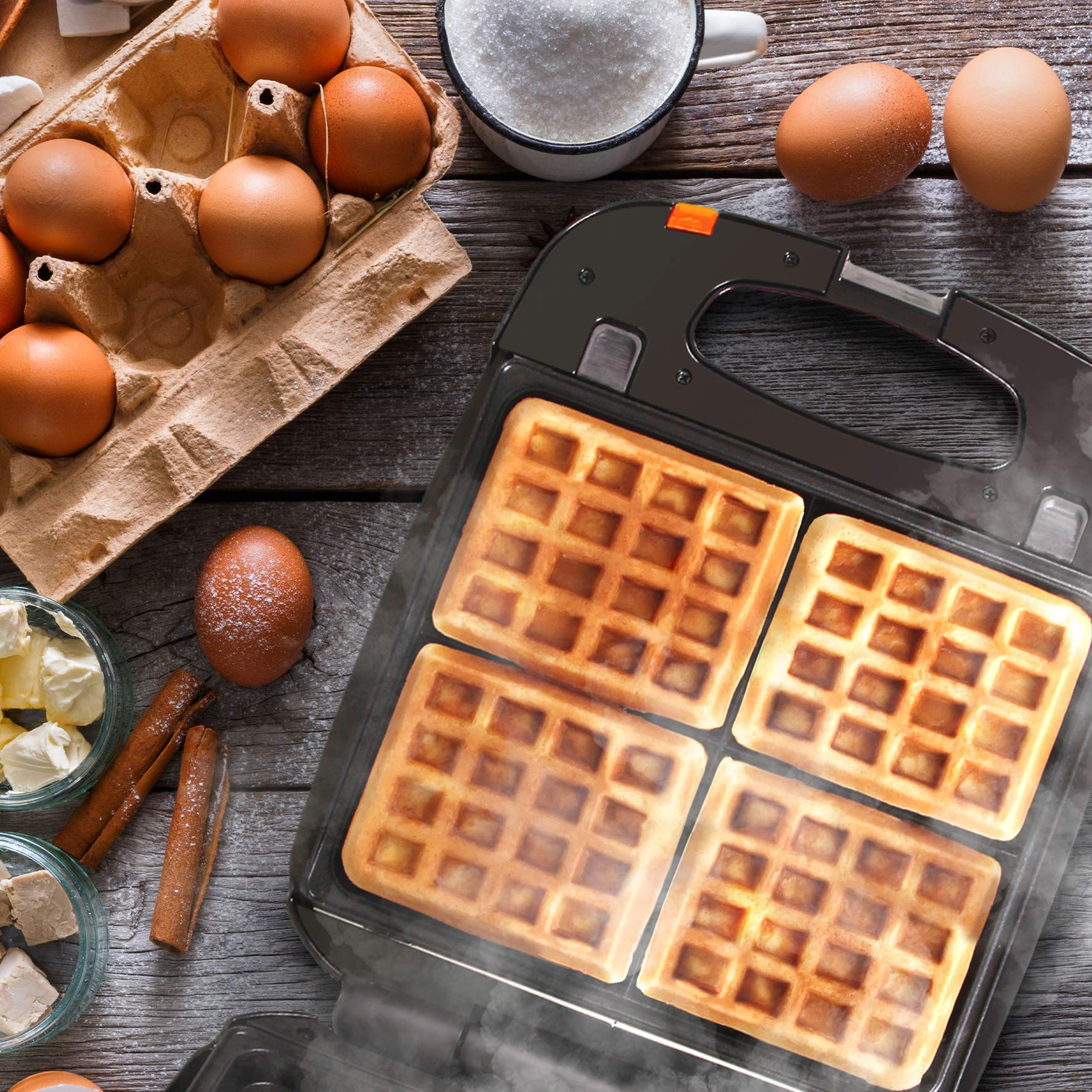 Waffeleisen mit vier Waffeln, Eiern, Butter, Zucker und Zimtstangen.