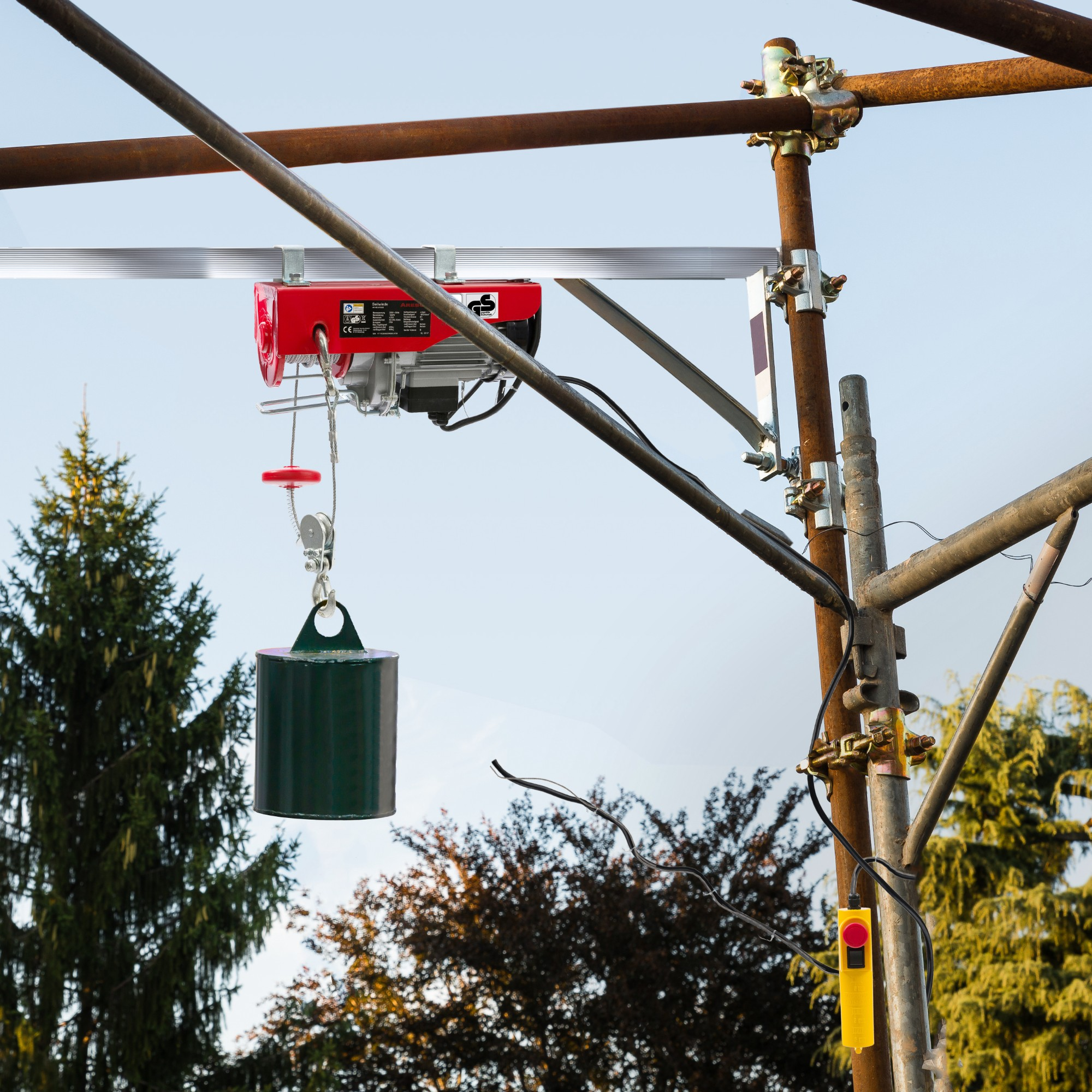Ein roter elektrischer Hebezug hebt ein grünes Gewicht an, das von einer Gerüstkonstruktion hängt.
