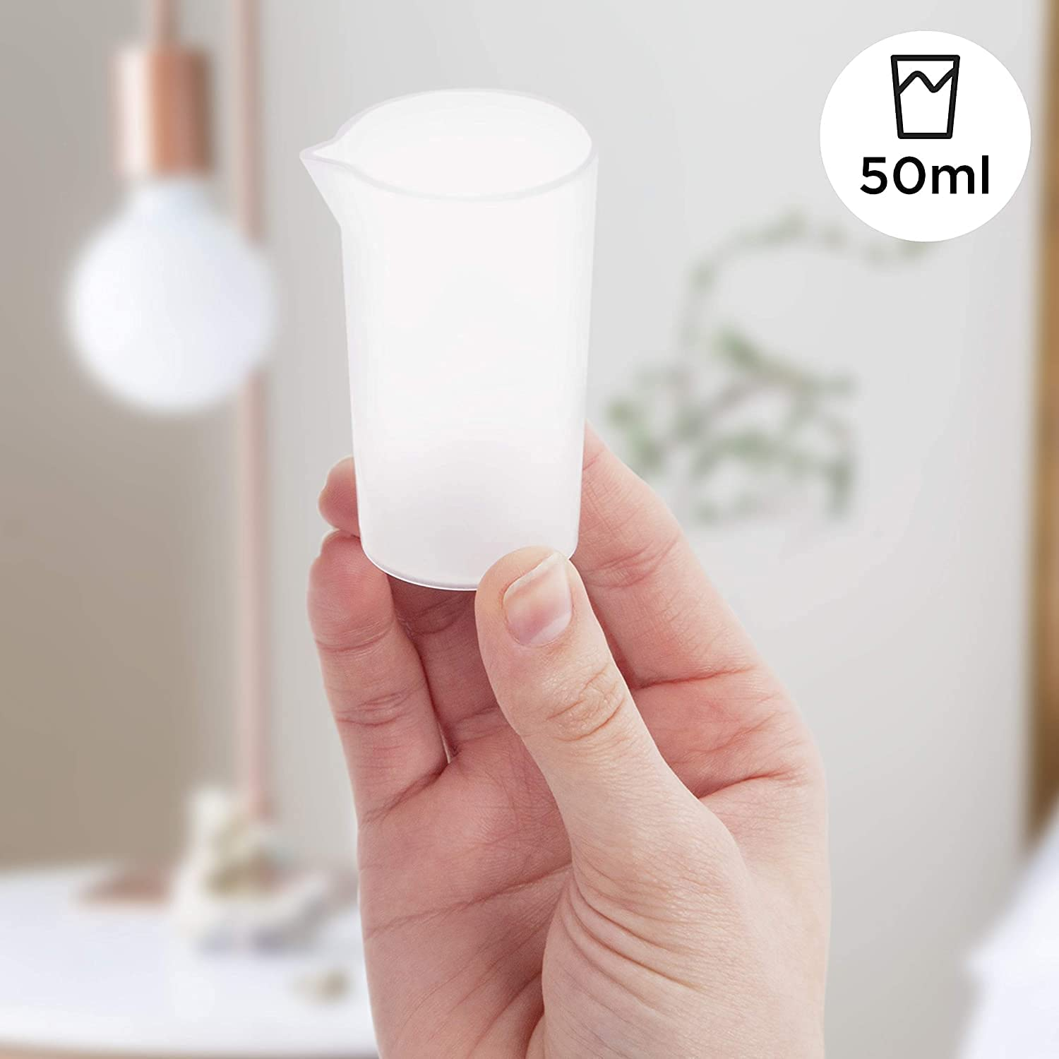 Ein klarer Messbecher, 50 ml, in der Hand gehalten, mit unscharfem Hintergrund und Licht.