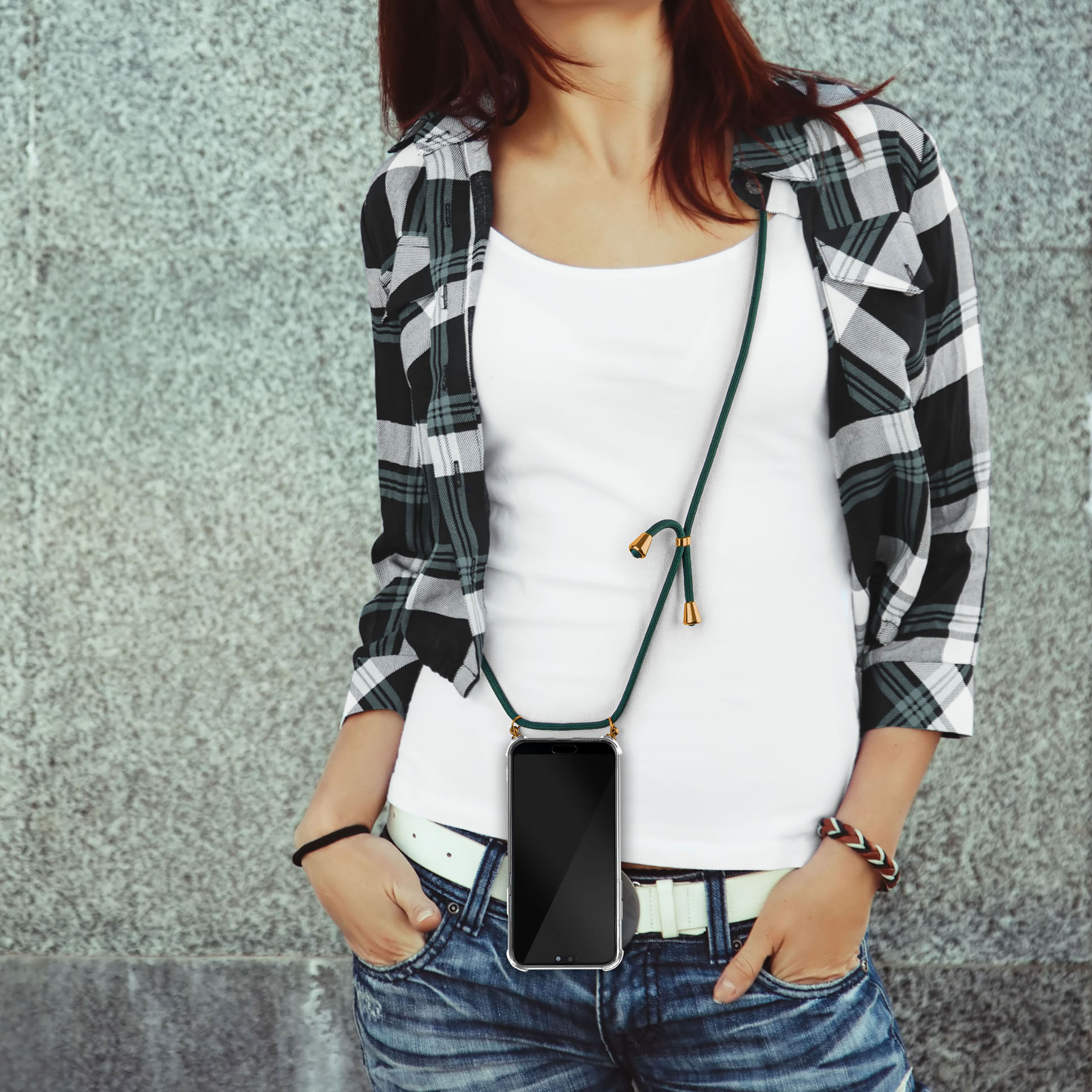 Frau in weißem Hemd, Jeans und kariertem Hemd, mit einem Telefon an einem grünen Riemen um den Hals.