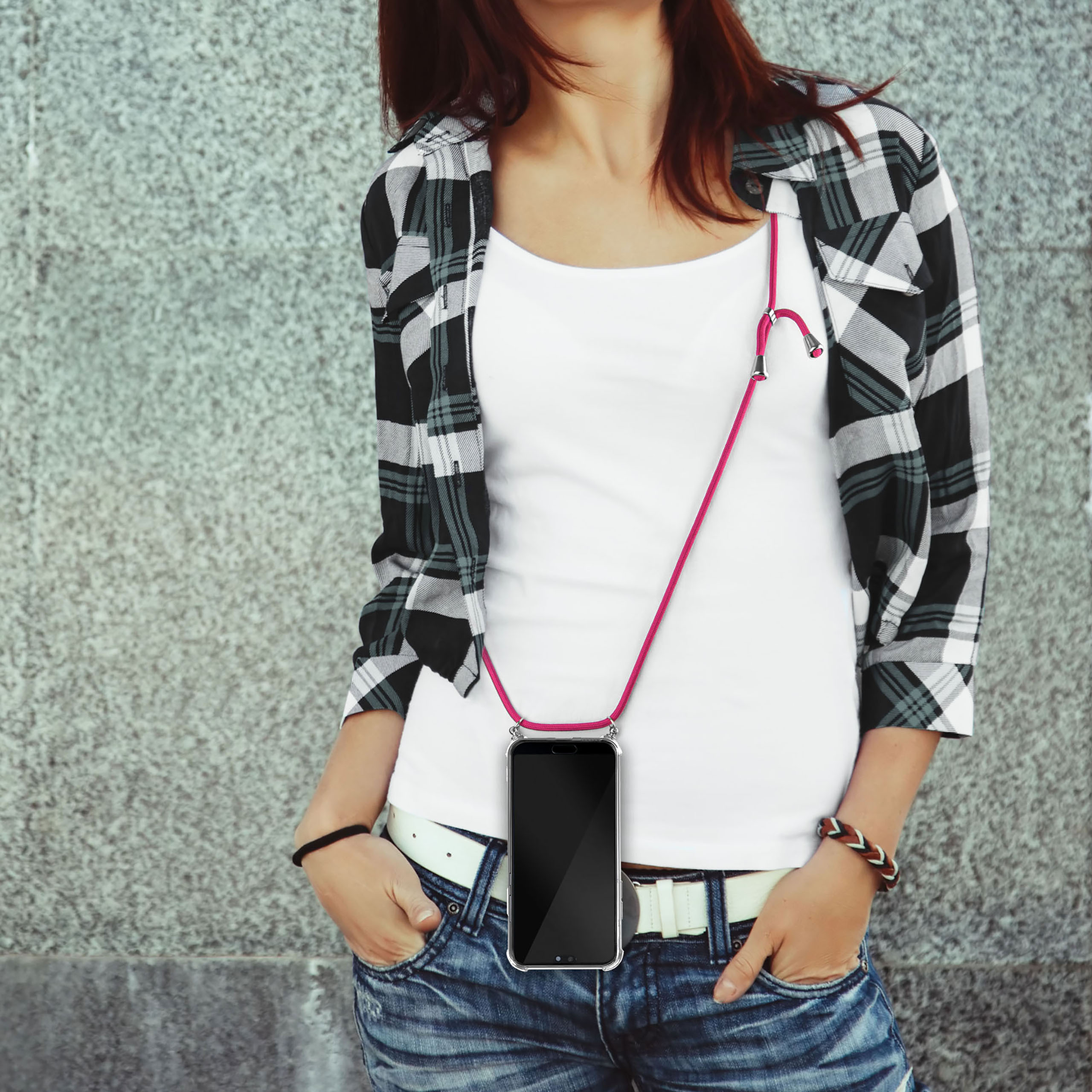 Eine Frau mit weißem Oberteil und kariertem Hemd, die ein Telefon mit rosa Band um den Hals hält.