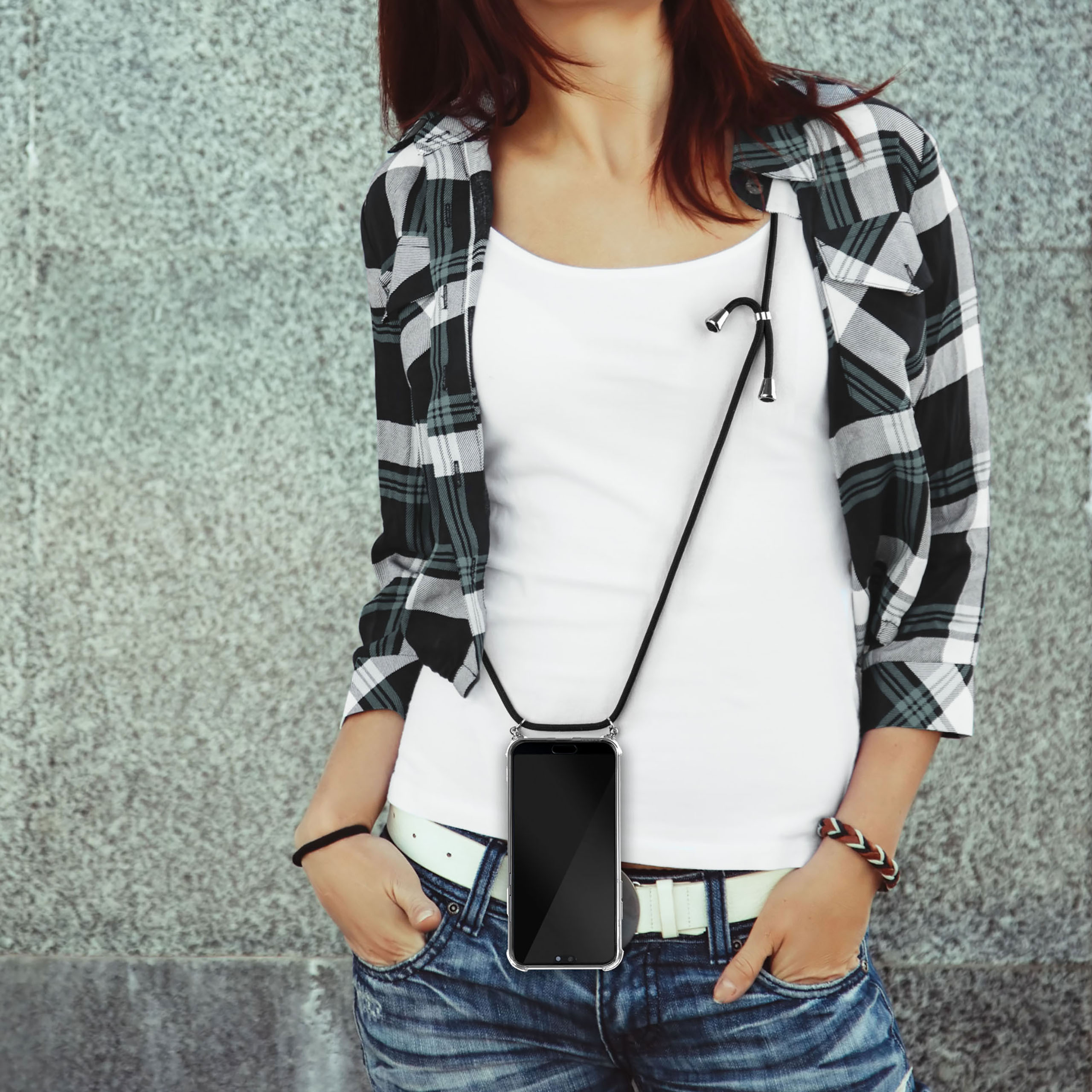 Frau mit einem Handy-Lanyard, die an einer grauen Wand steht.