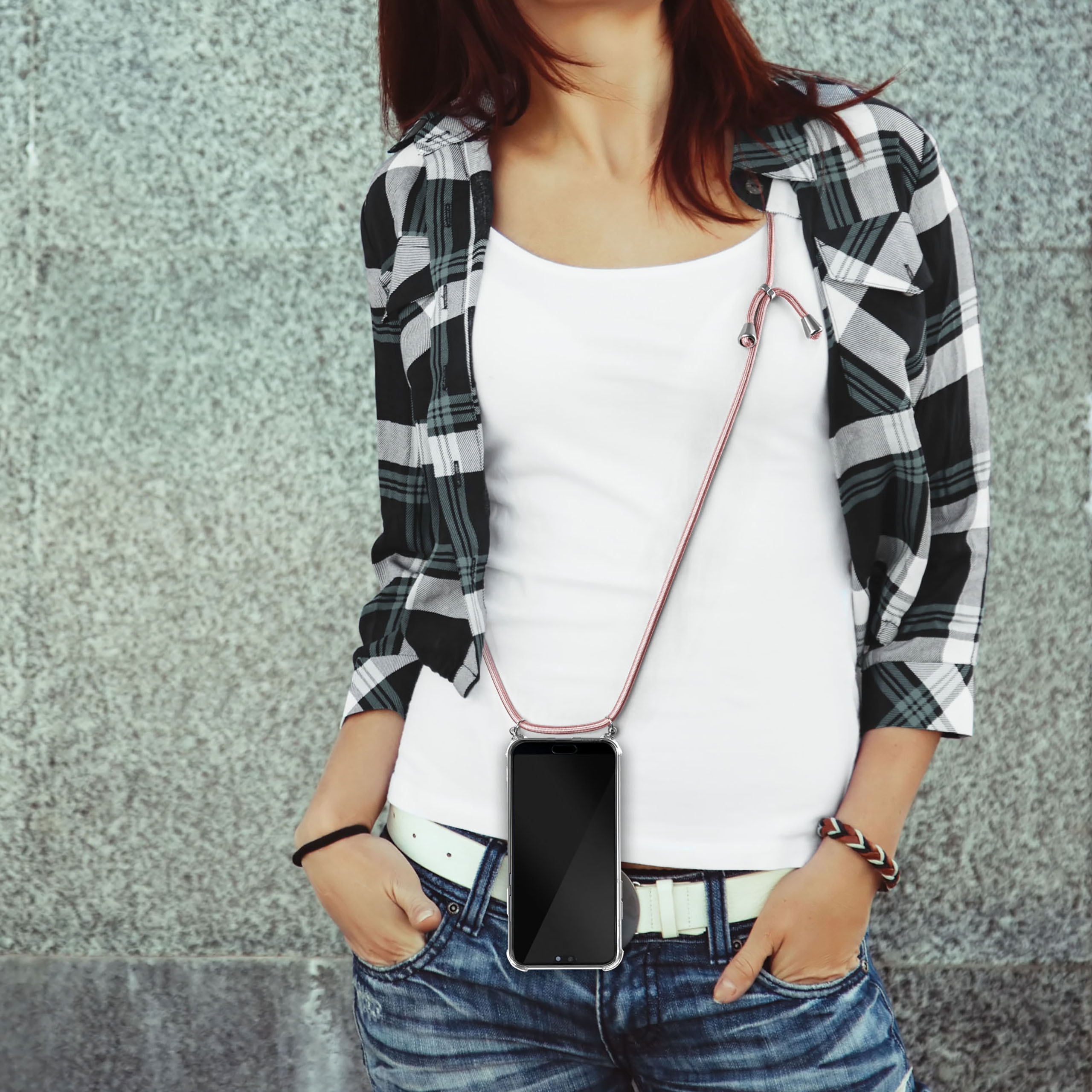 Eine Frau mit weißem Hemd, Jeans und kariertem Hemd, die ein Telefon mit Lanyard hält.