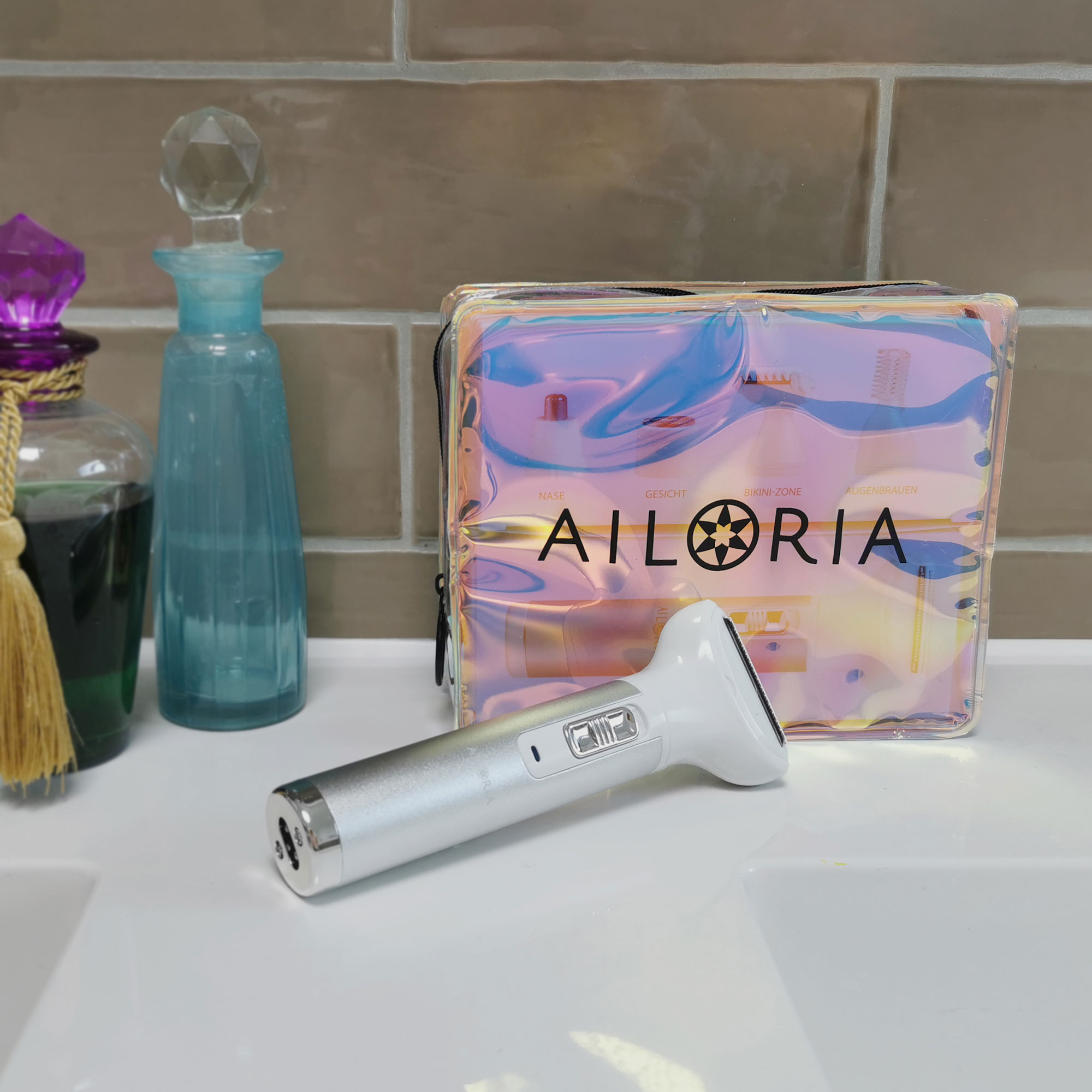 AILORIA-Produkt mit weissem und silbernem Gerät. Rosa und irisierende Tasche. Weisse Oberfläche, braune Fliesenwand.