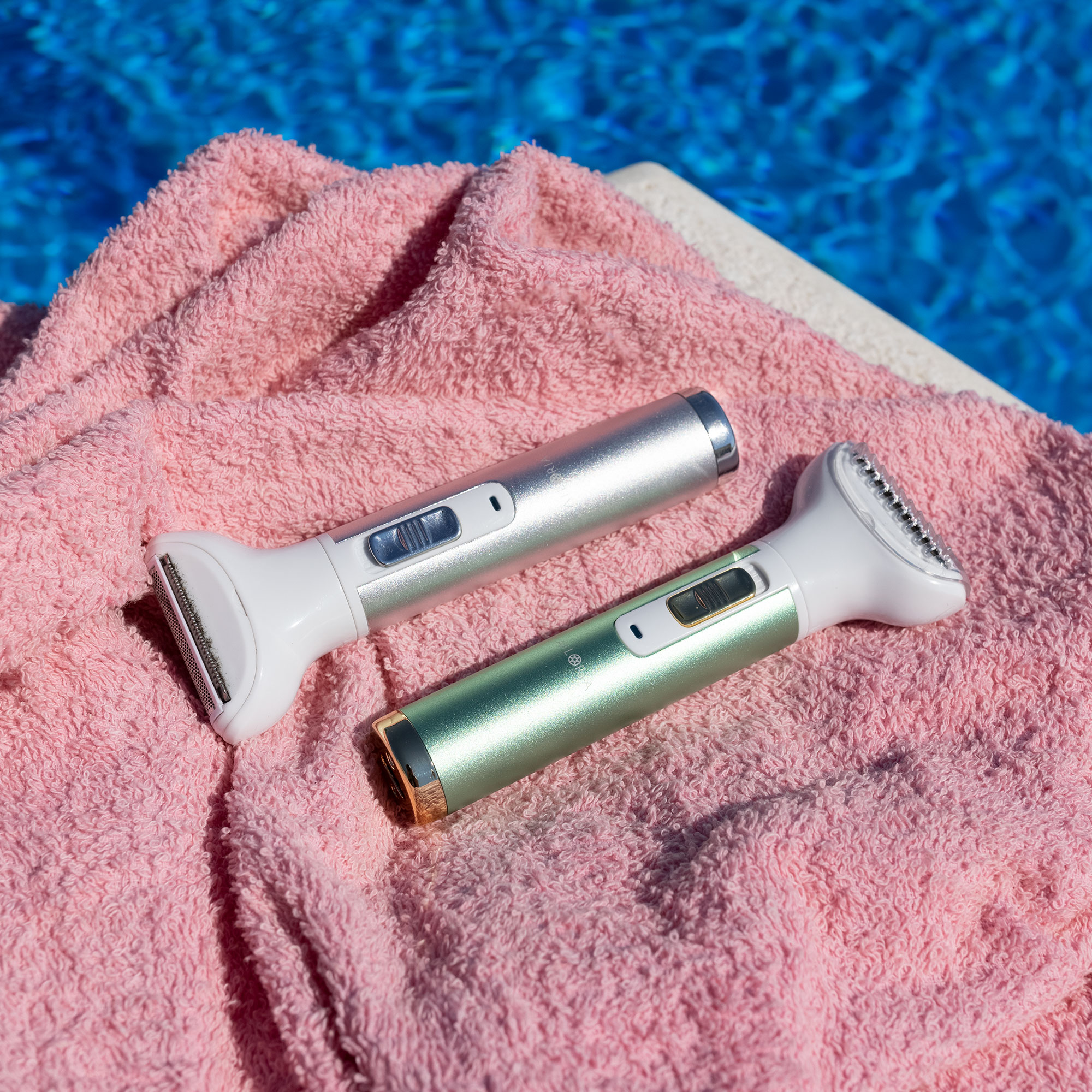Zwei elektrische Rasierer auf einem rosa Handtuch, neben einem blauen Pool.