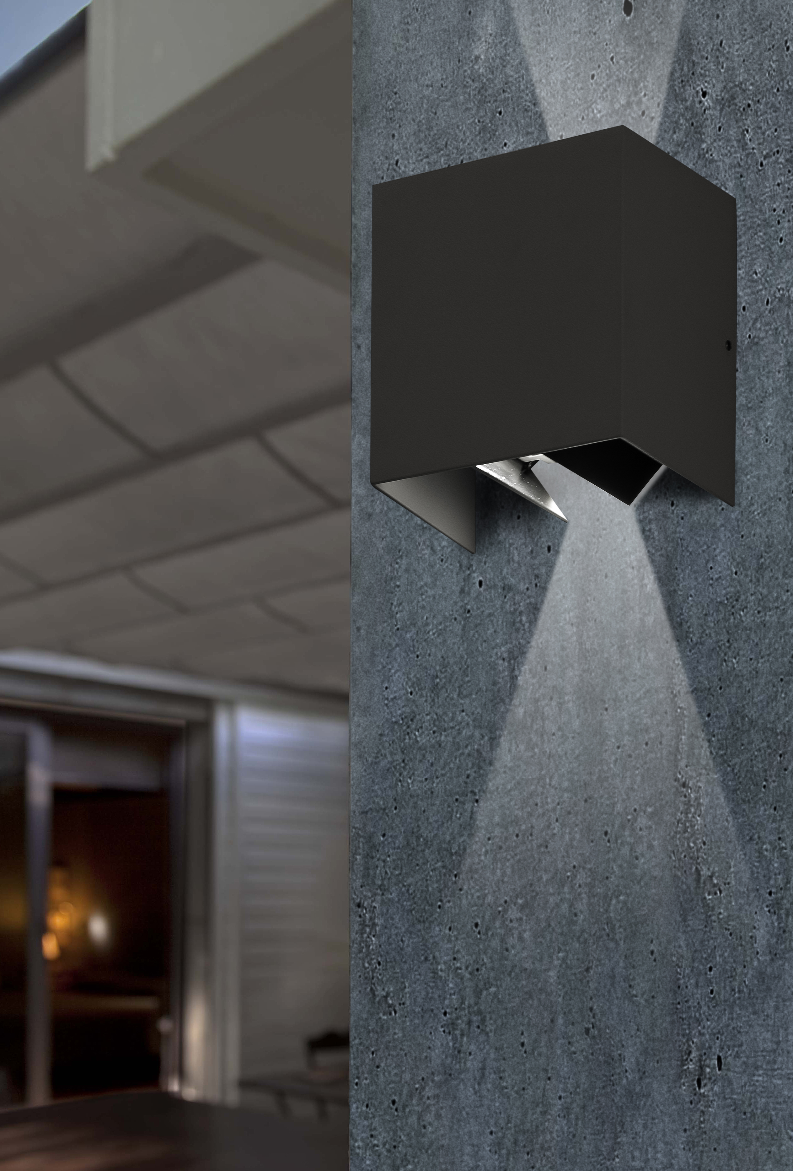 Un apparecchio di illuminazione a forma di cubo nero montato su un muro di cemento. La luce brilla verso il basso.