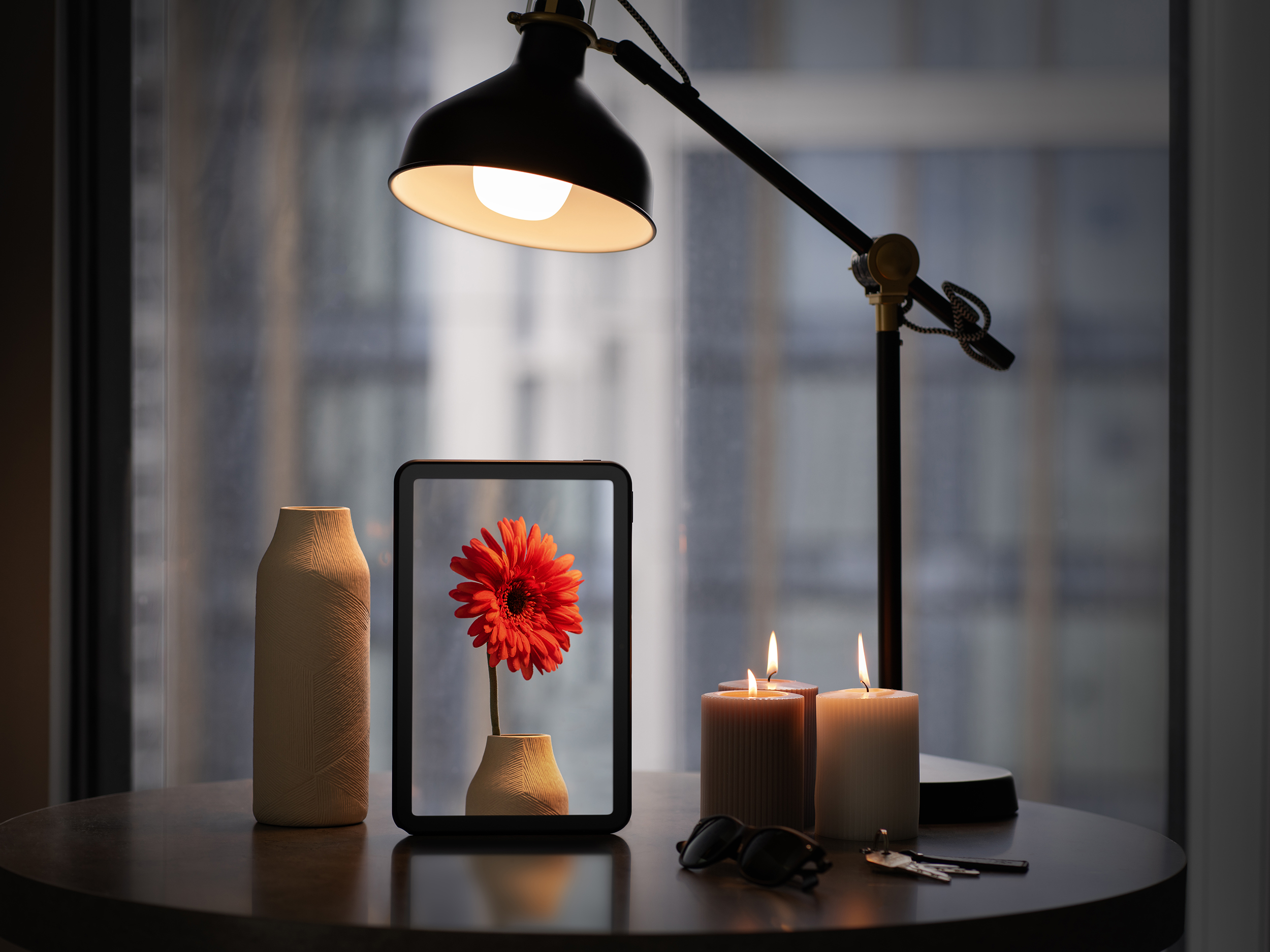 Tisch mit Blume im Rahmen, Kerzen, Lampe und Brille.