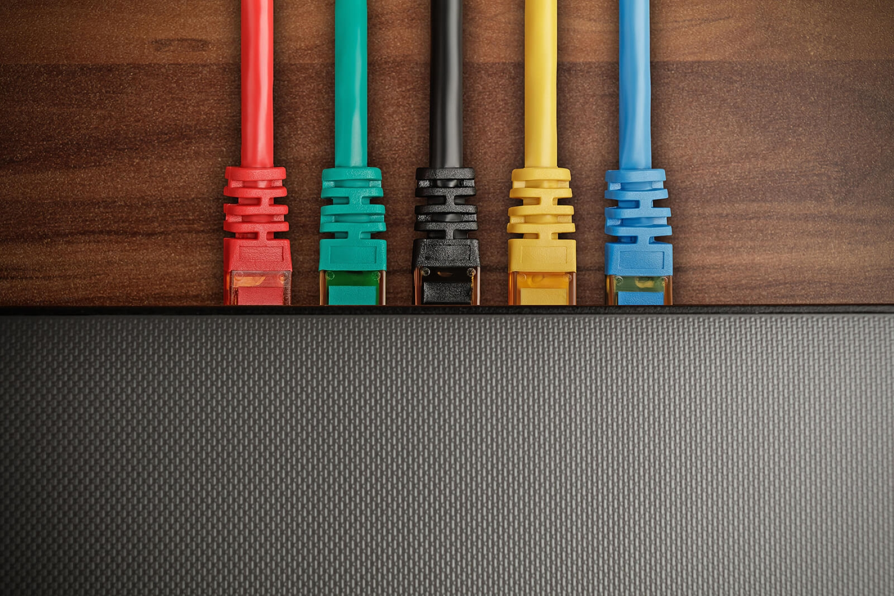 Fünf farbige Ethernet-Kabel, die in ein schwarzes Gerät auf einer Holzoberfläche gesteckt sind.