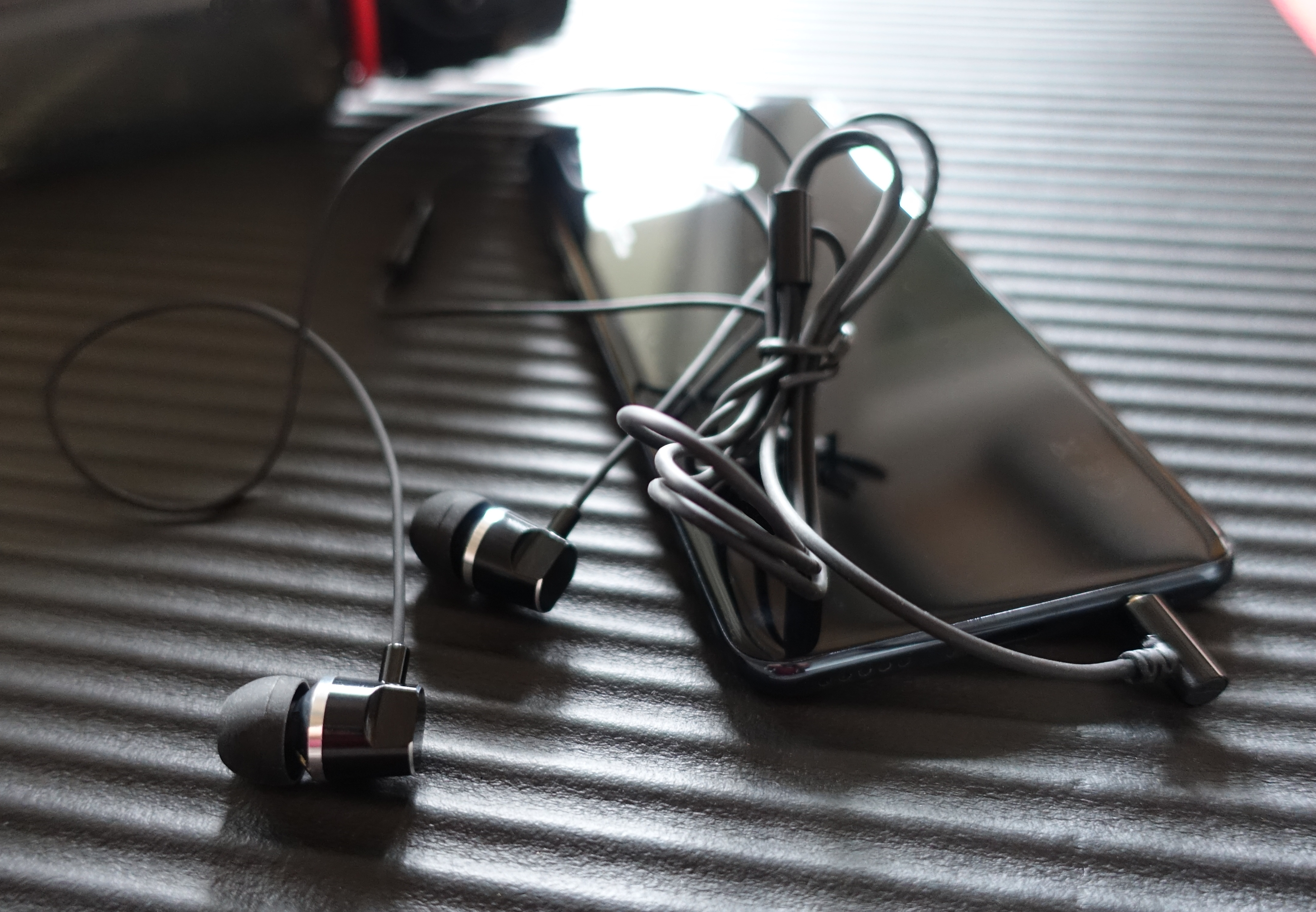 Auricolari e cavo neri vicino a uno smartphone nero su una superficie strutturata.