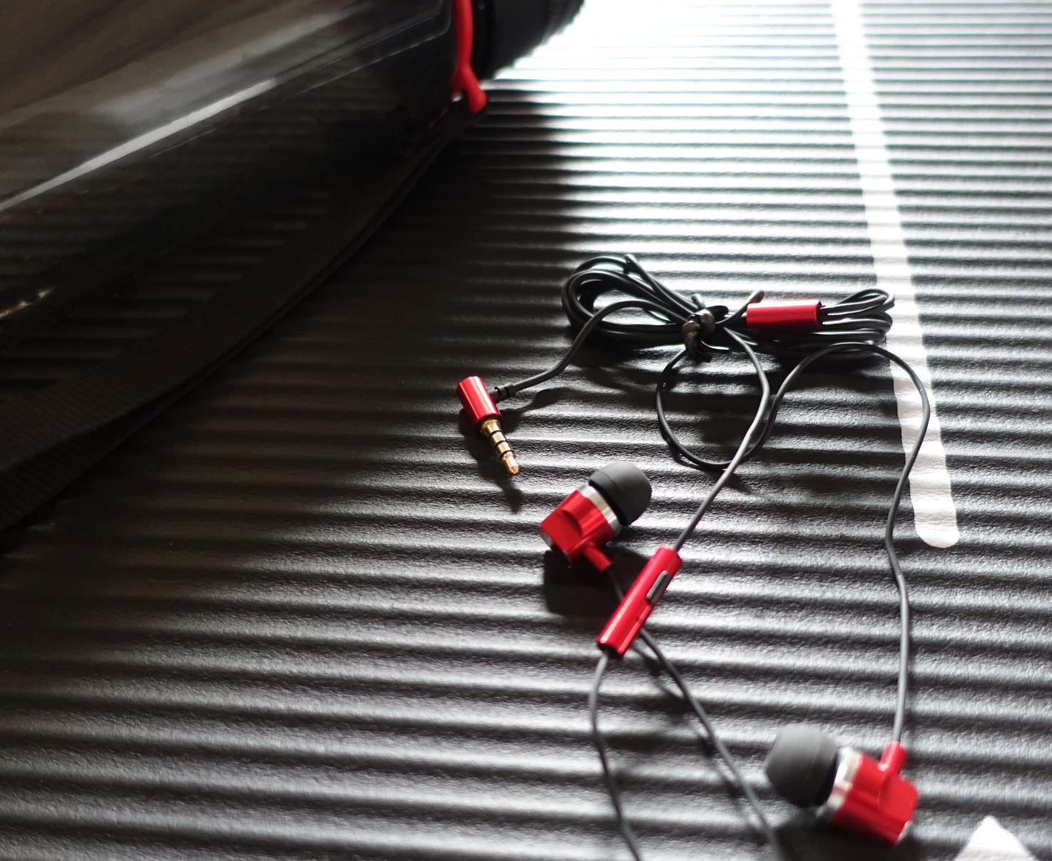 Rote Ohrhörer mit schwarzem Kabel und rotem Stecker, die auf einer strukturierten schwarzen Oberfläche liegen.