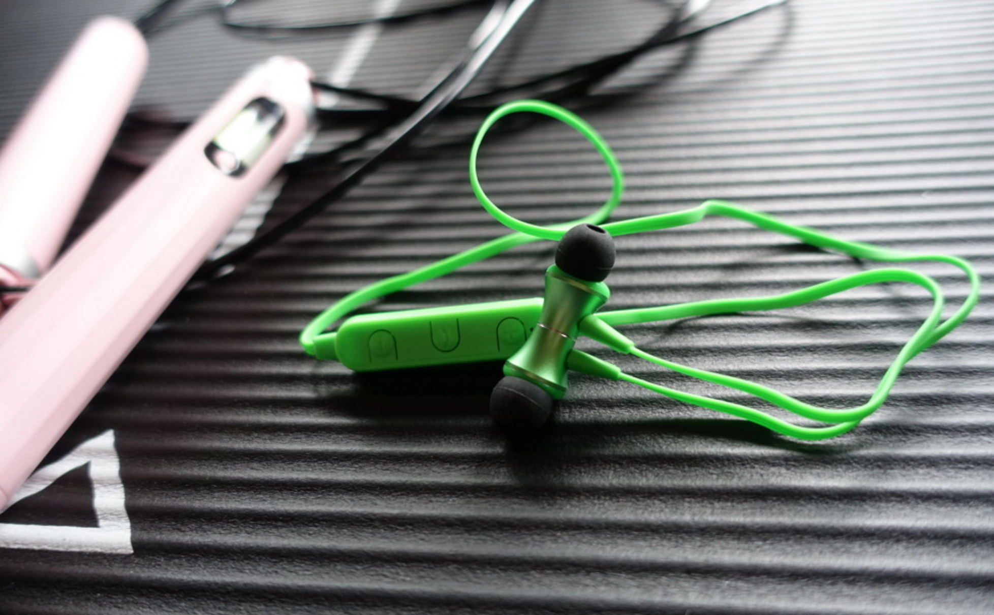 Kopfhörer mit grünem Kabel, schwarzen Ohrhörern und rosa Bedienelement. Auf strukturierter Oberfläche.