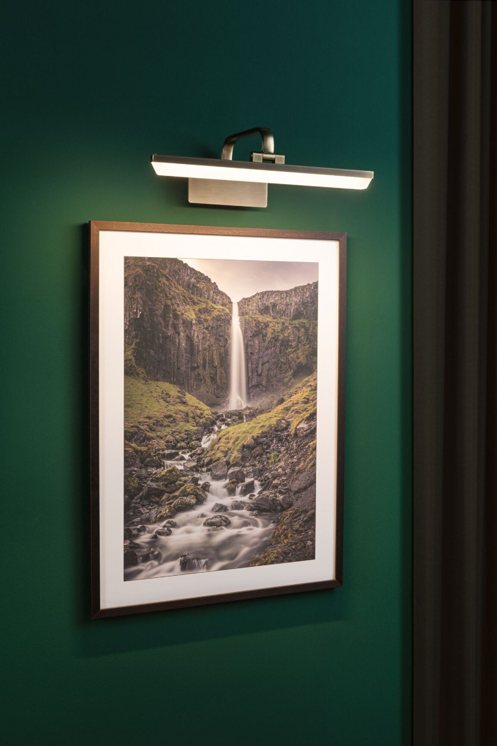 Obraz wodospadu na zielonej ścianie, oświetlony małą lampą.