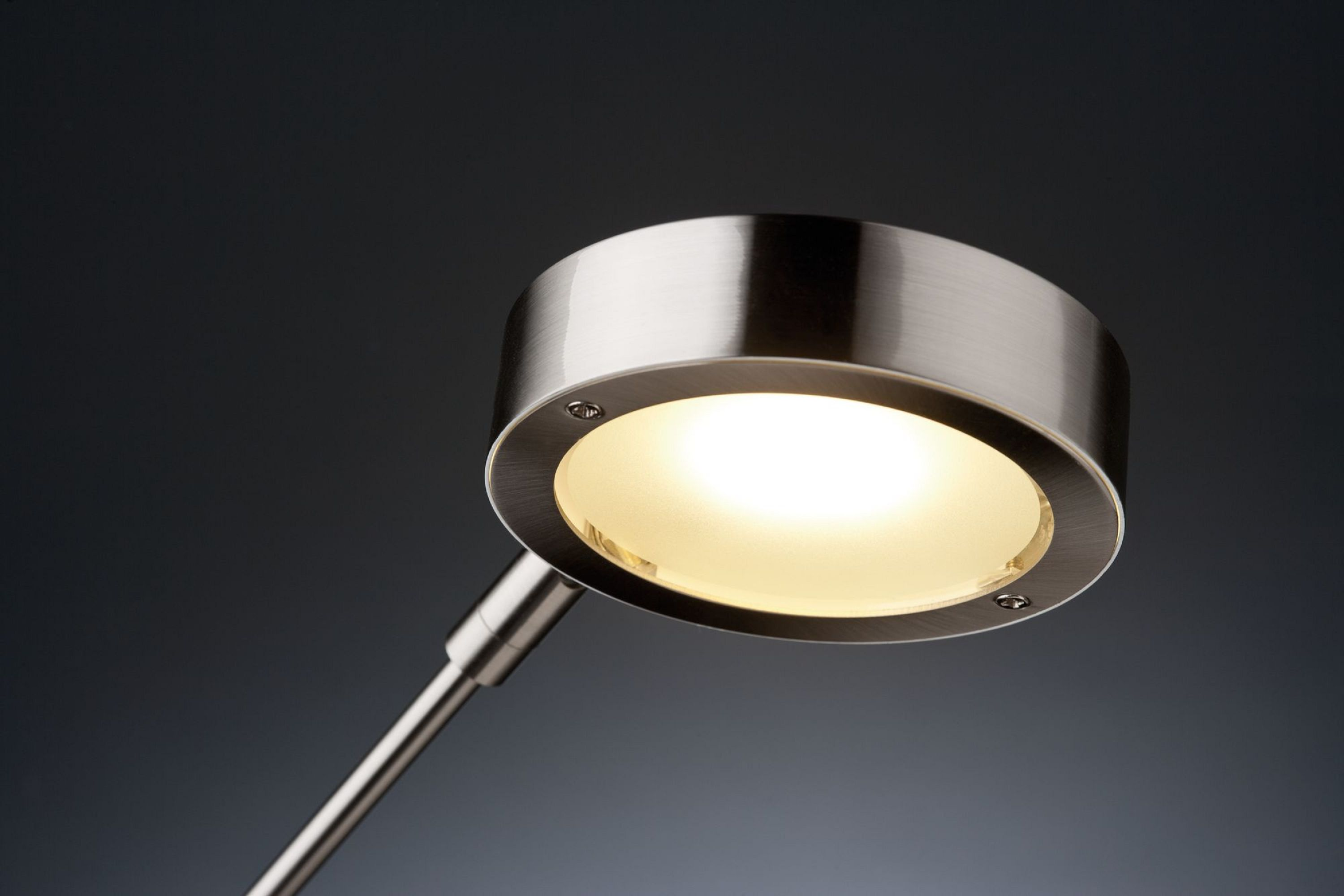 Zbliżenie nowoczesnej, srebrnej głowicy lampy z ciepłym światłem na ciemnoszarym tle.