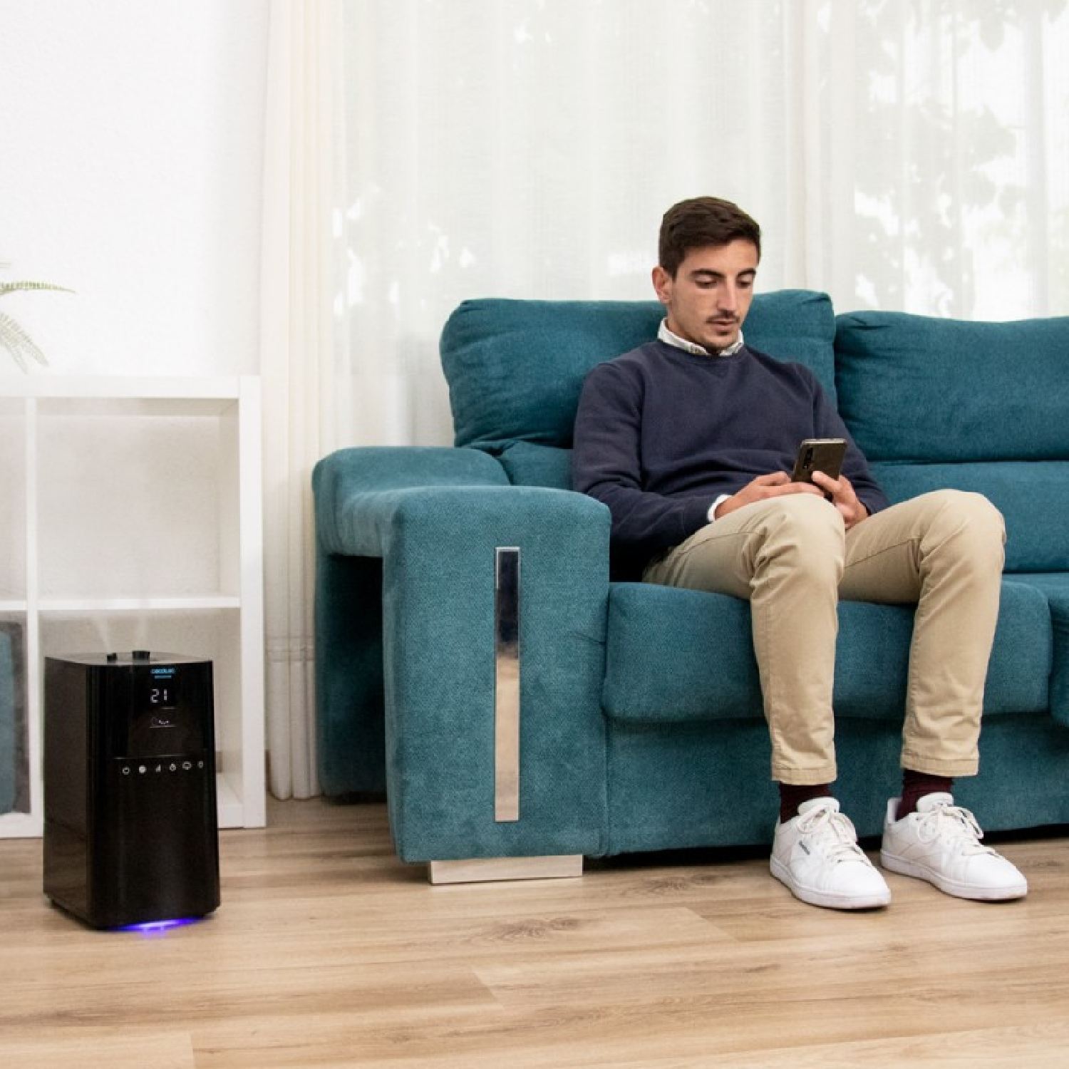 Un uomo è seduto su un divano verde acqua che guarda il suo telefono, con un purificatore d'aria nero.