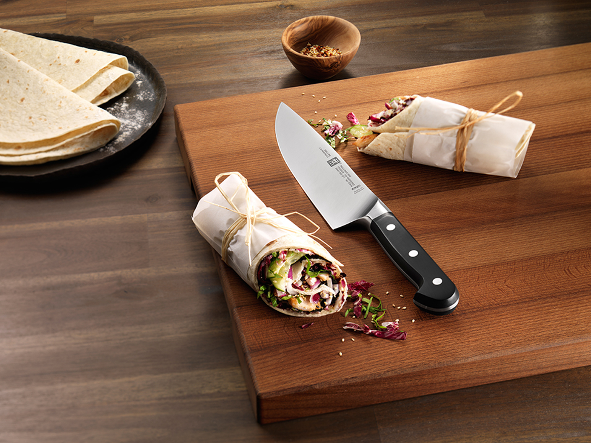 Nóż na drewnianej desce do krojenia, zawijane jedzenie.