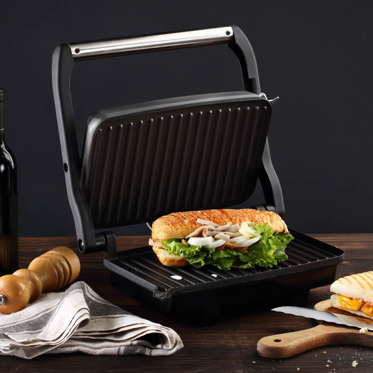 Pressa per panini aperta con un panino dentro. Panino con lattuga, cipolle e pomodori.