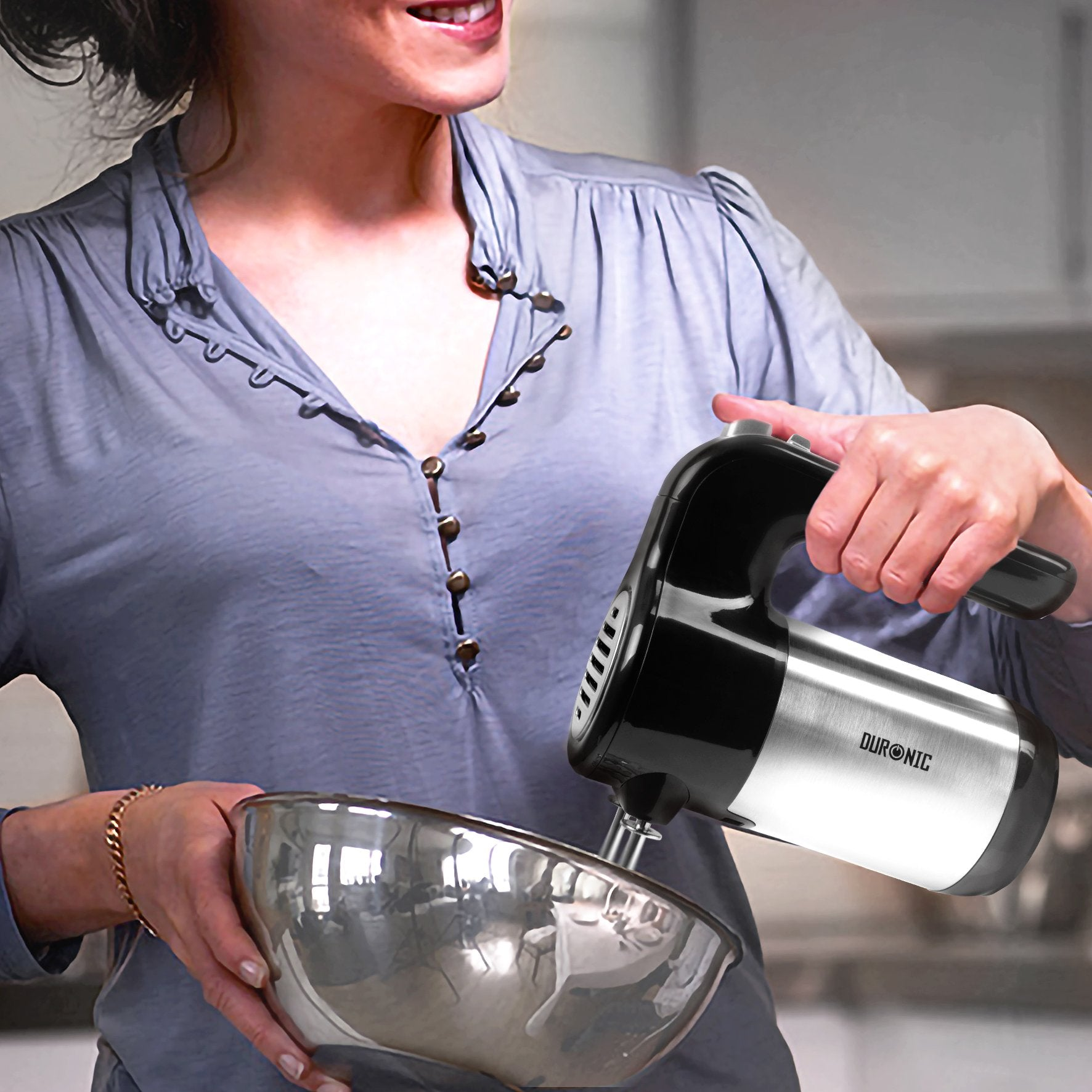 Frau benutzt Handmixer in der Küche. Silberne Schüssel und schwarz-silberner Mixer.