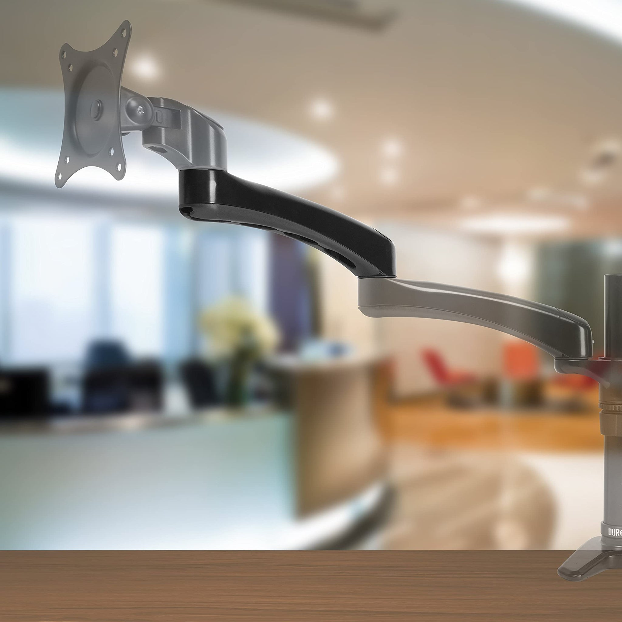 Monitorarm auf einem Holztisch, mit unscharfem Bürohintergrund.
