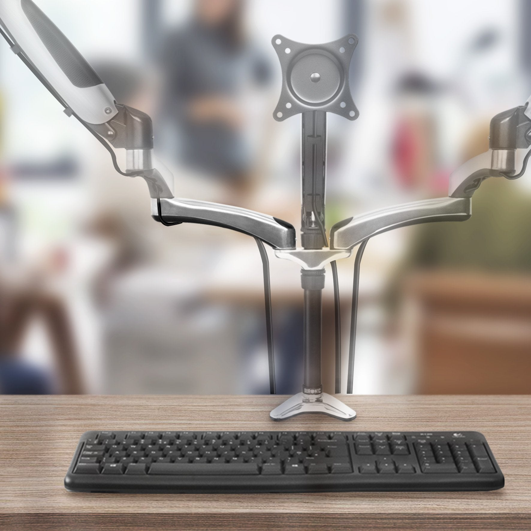Monitorständer und Tastatur auf einem Holzschreibtisch, mit verschwommenem Bürohintergrund.