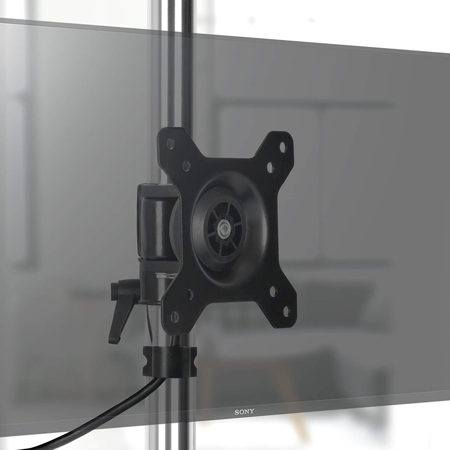 Primer plano de un soporte de monitor negro. Está montado en un poste plateado con una pantalla en el fondo.