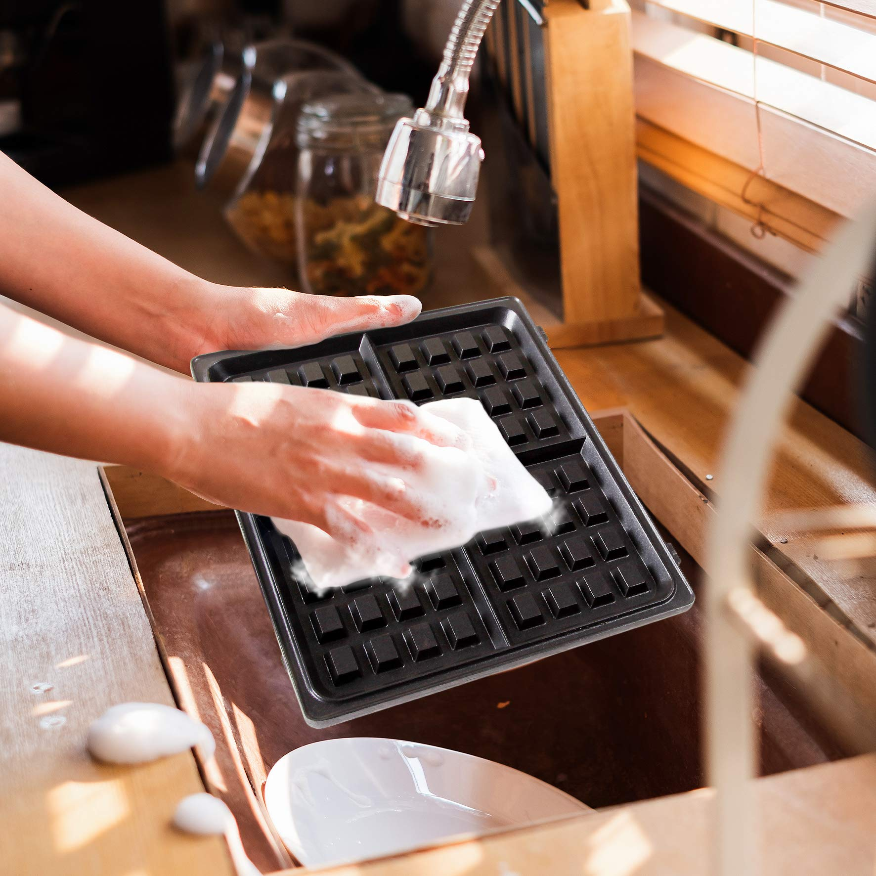 Person reinigt Waffeleisen in einem Waschbecken. Seifenwasser und weißer Schwamm.