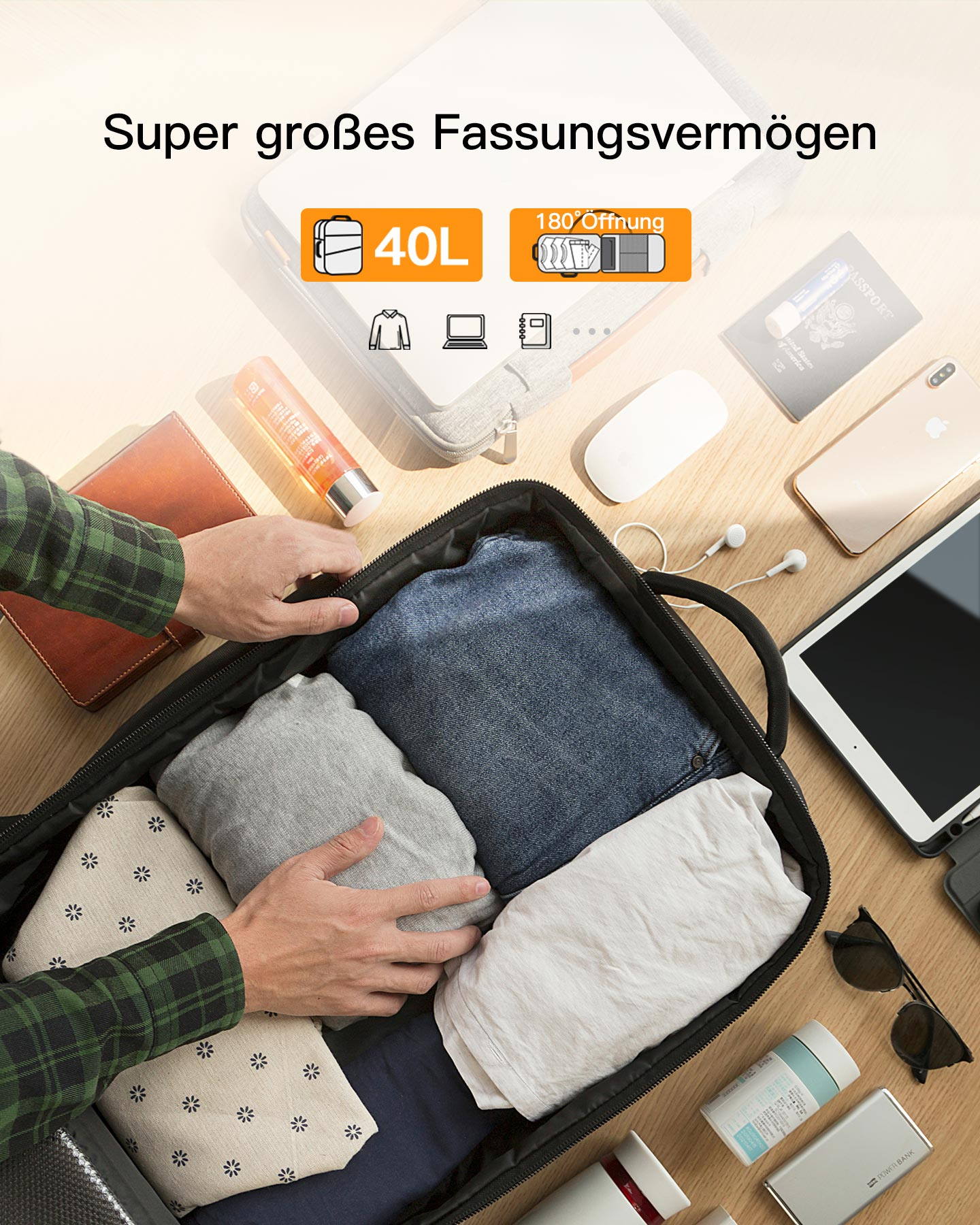 Hände packen eine Tasche mit Kleidung, Pass, Telefon, Tablet und Zubehör auf einem Tisch.