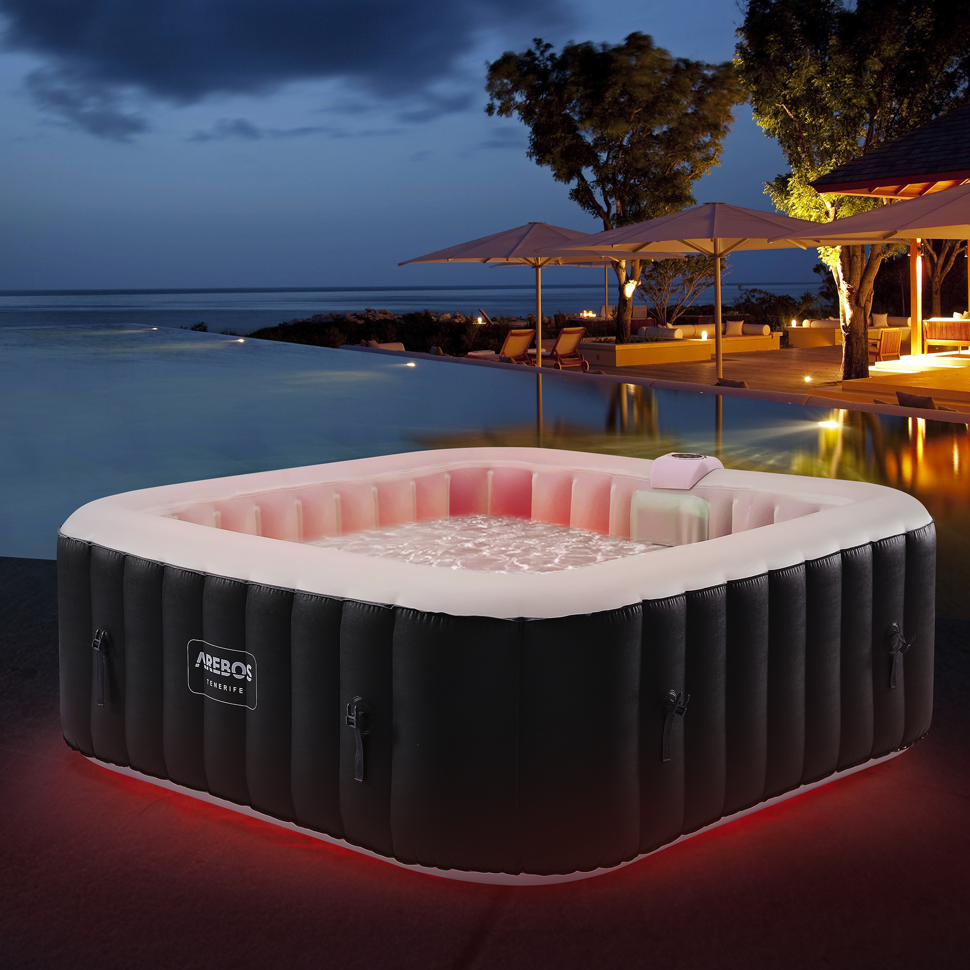 Nachtaufnahme eines aufblasbaren Whirlpools mit rotem Licht unter sternenklarem Himmel. Pool und Palmen sichtbar.
