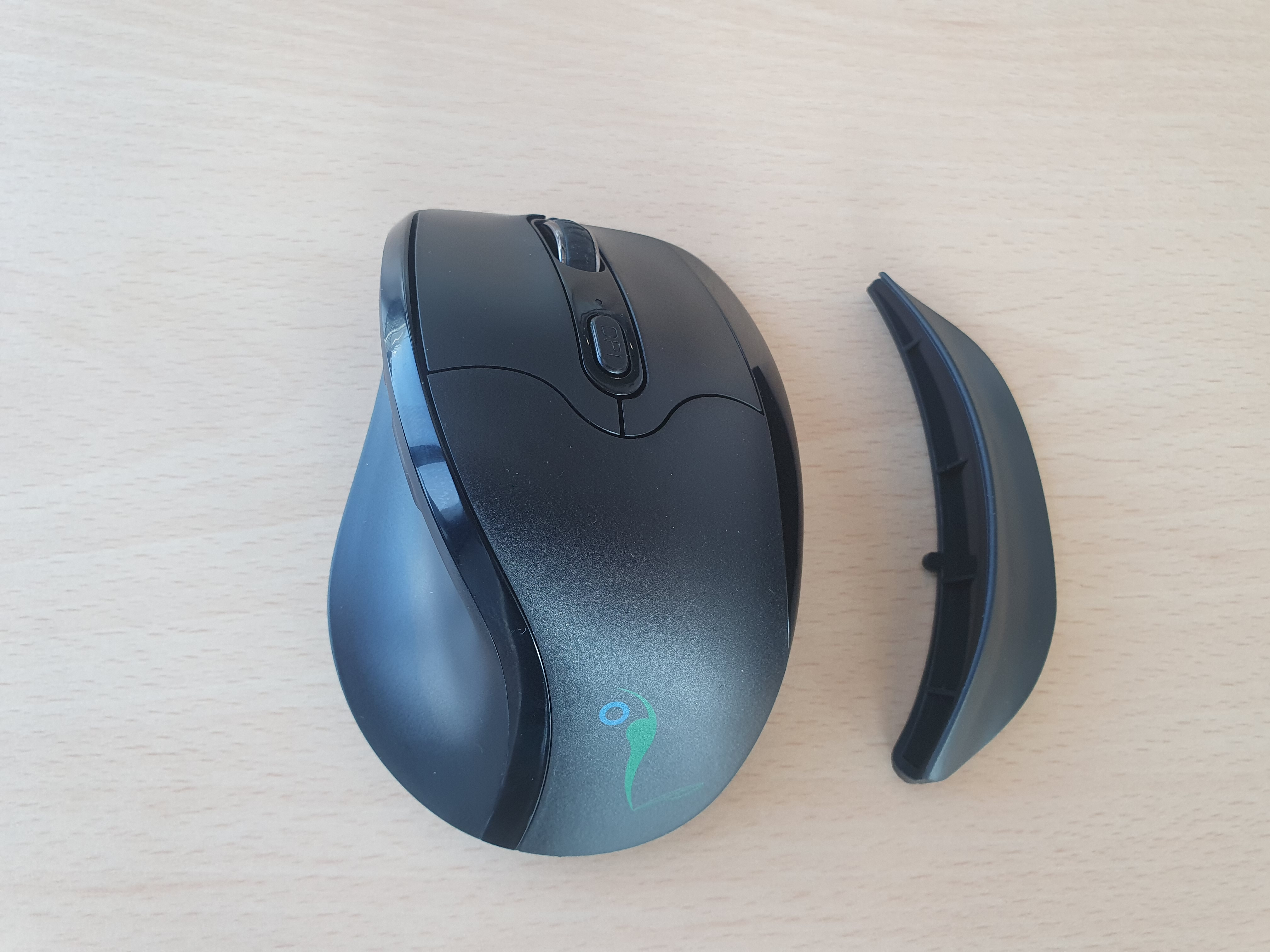 Eine schwarze Computermaus mit einem zusätzlichen Teil auf einer Holzoberfläche. Der Hintergrund ist ein Holzschreibtisch.