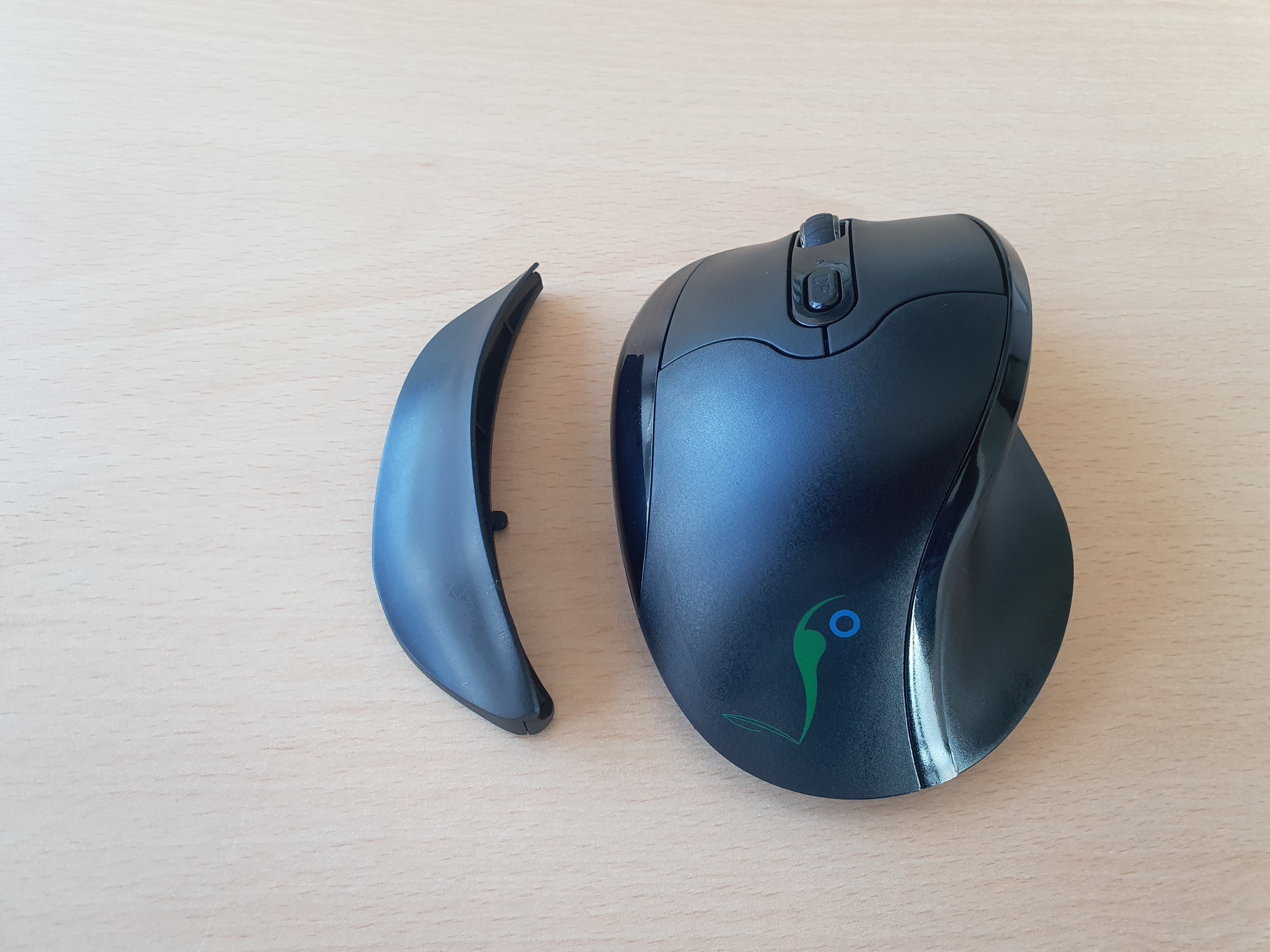 Eine Computermaus mit abgetrenntem Seitenteil auf einer Holzoberfläche. Die Maus ist schwarz.