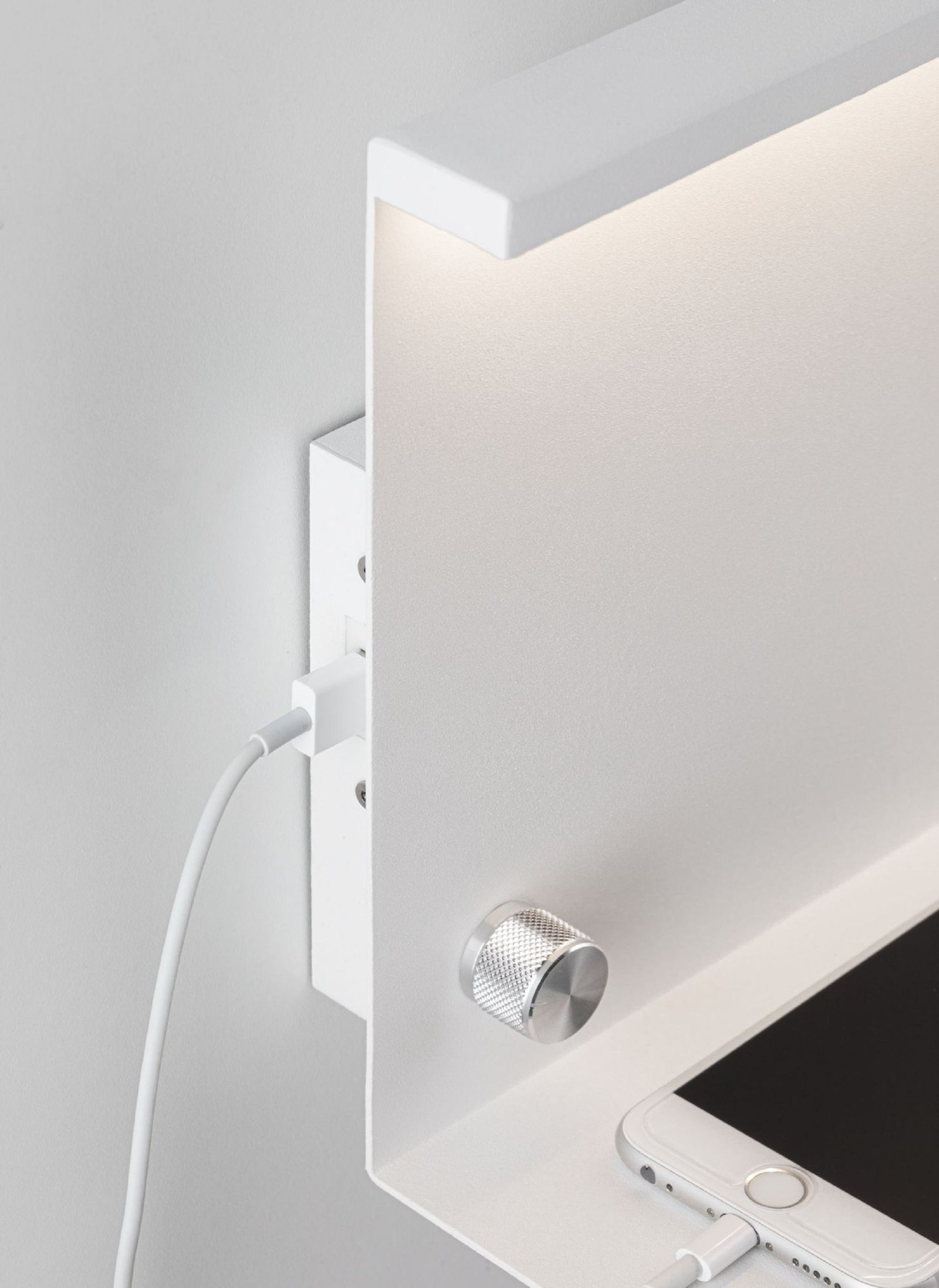 Ein weißes Wandregal mit USB-Anschluss und einem darauf ladenden Telefon. Die Oberseite hat ein Licht.