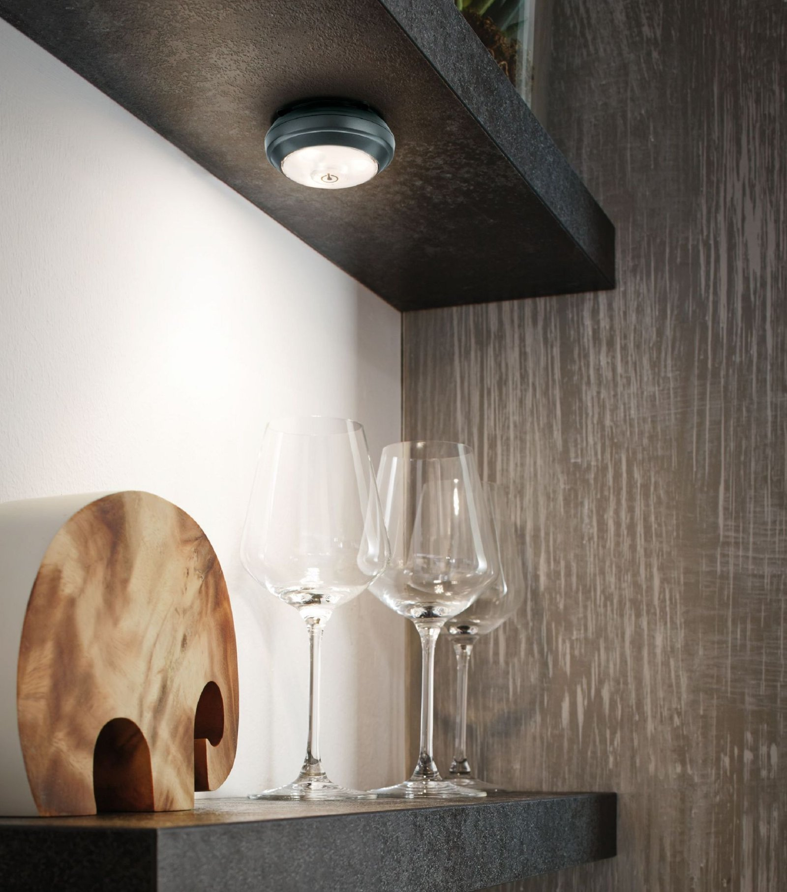 Ein schwach beleuchtetes Küchenregal mit einer kleinen LED-Leuchte, Weingläsern und einem dekorativen Holzobjekt.