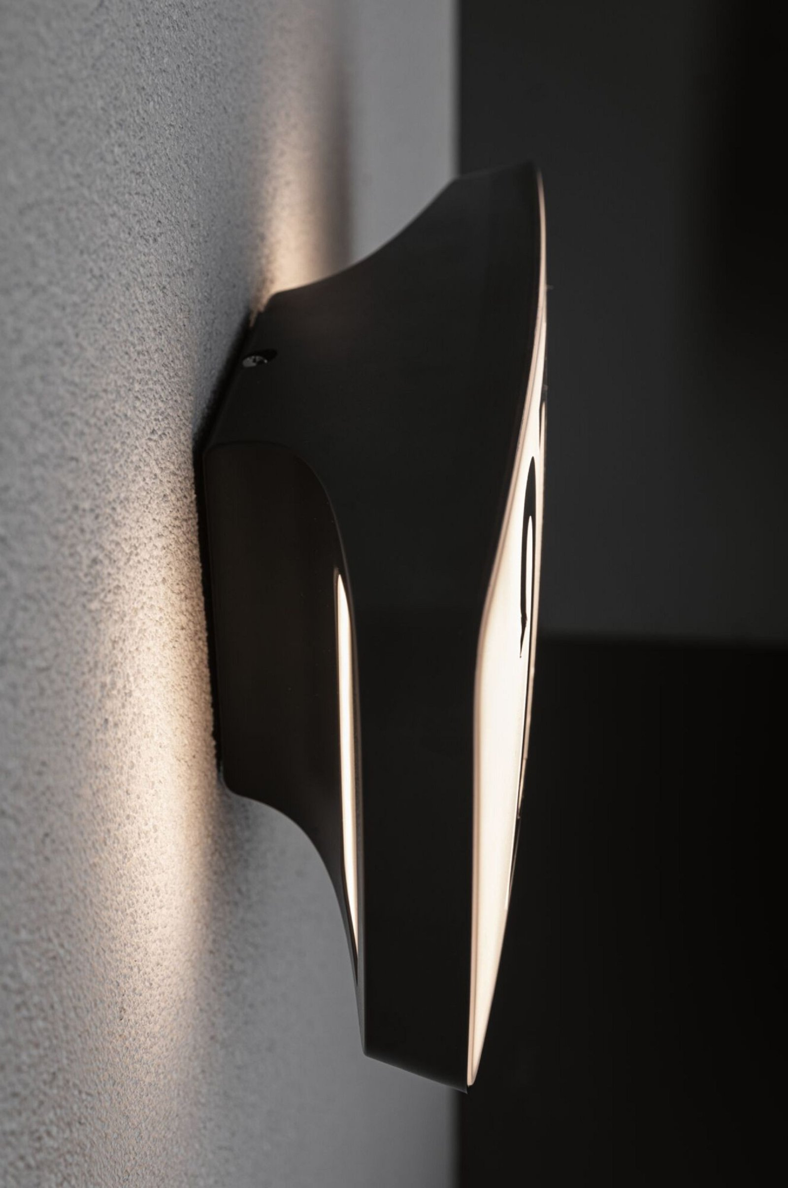 Czarno-biała lampa ścienna, ustawiona pod kątem do szarej ściany, z świecącym światłem.