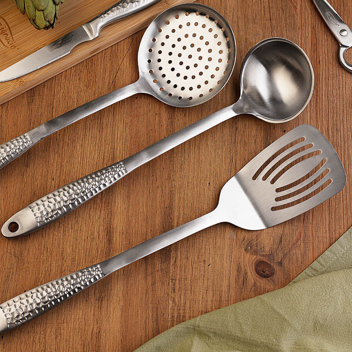 Utensilios de cocina: cuchara ranurada, cucharón y espátula sobre madera.