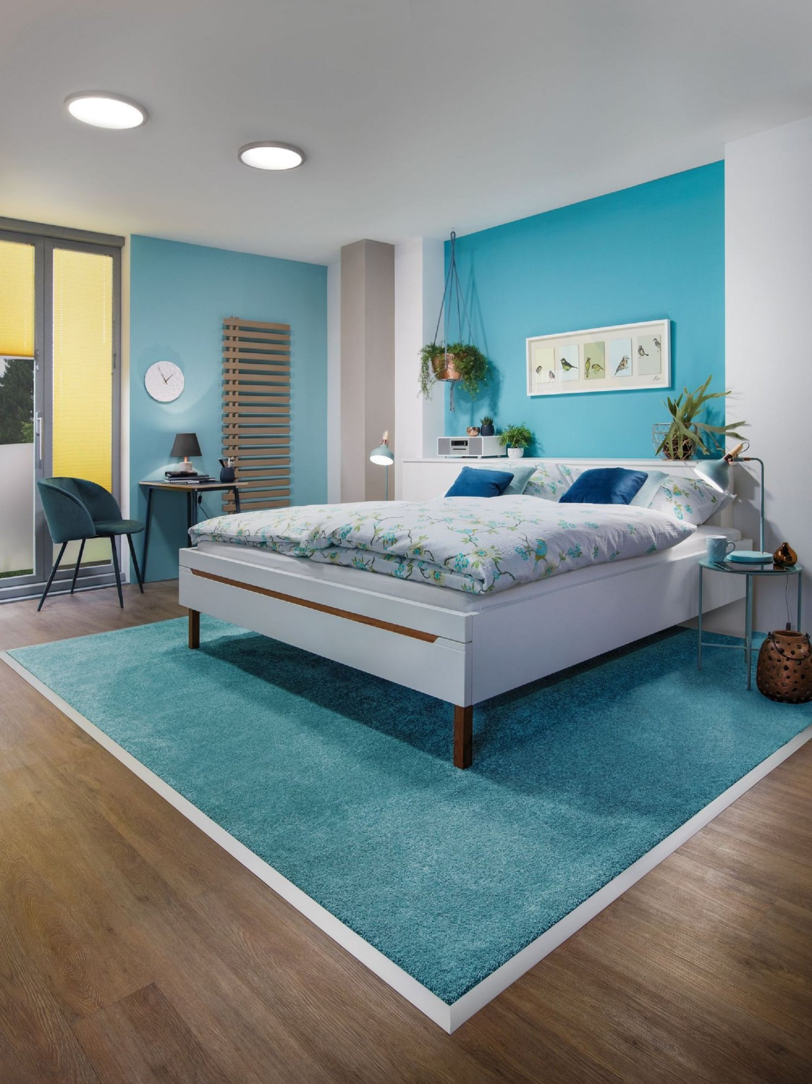 Camera da letto con letto, tappeto e piante contro un muro blu.
