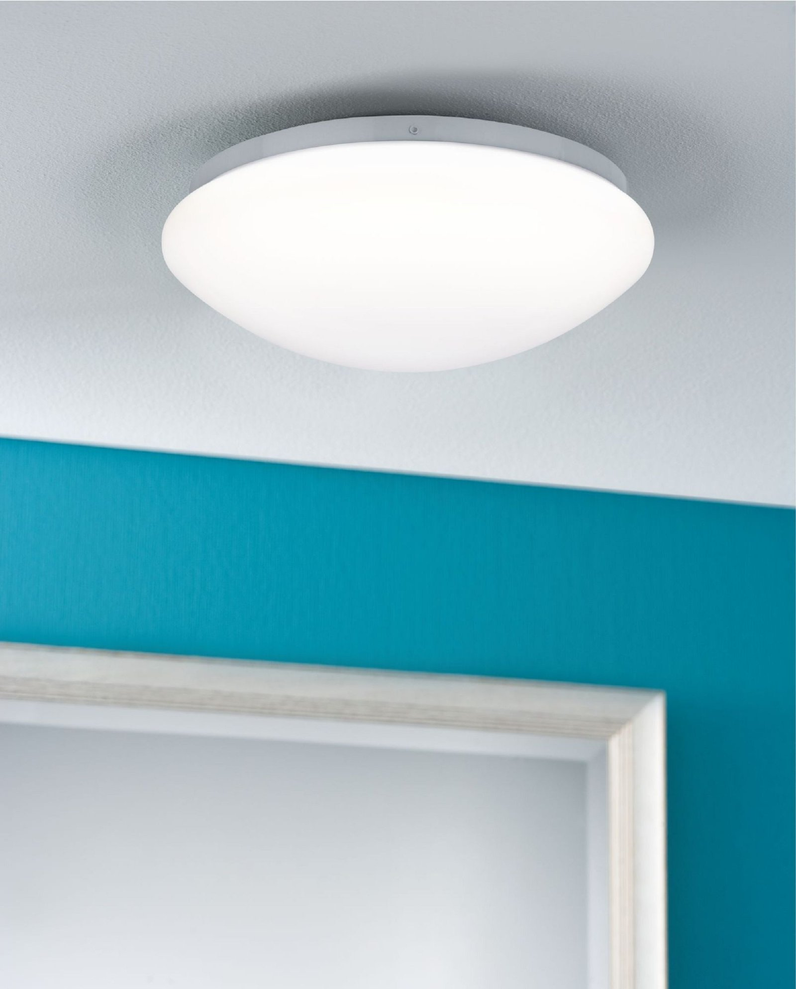 Eine weiße Deckenlampe an einer weißen Decke, über einer blauen Wand und weißem Türrahmen.