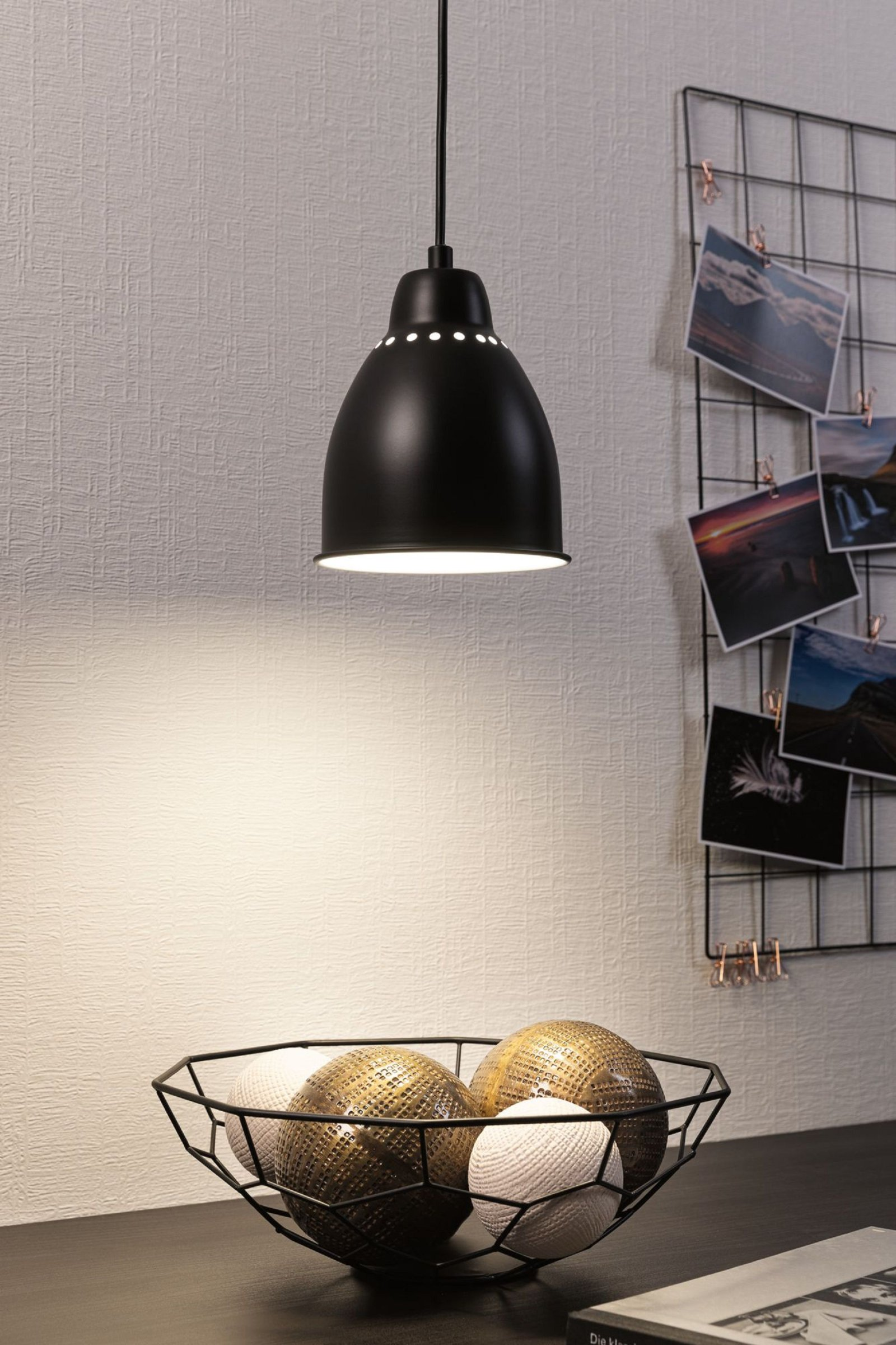 Czarna lampa wisząca nad stołem z miską kulek. Ściana ma kwiatowy wzór.