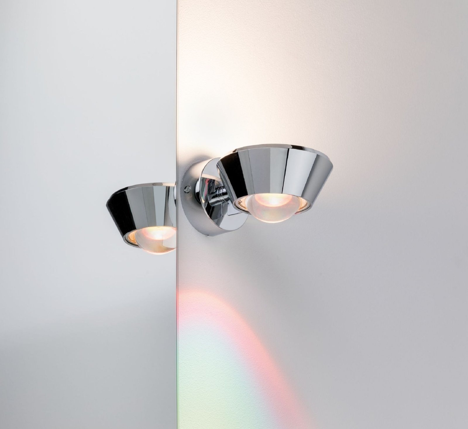 Zwei verchromte, schalenförmige Leuchten an der Wand, die einen Regenbogen reflektieren.