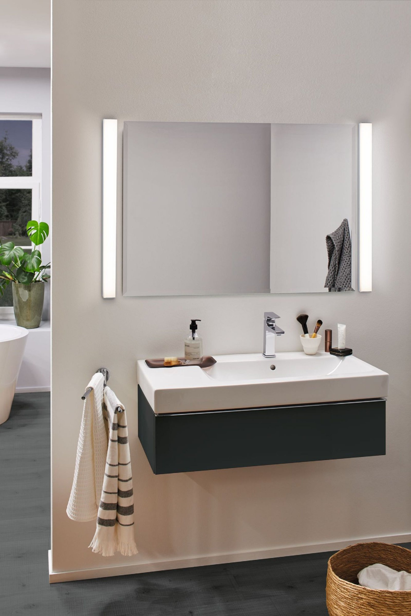 Scène de salle de bain avec miroir, lavabo, robinet et accessoires. Une serviette est accrochée.