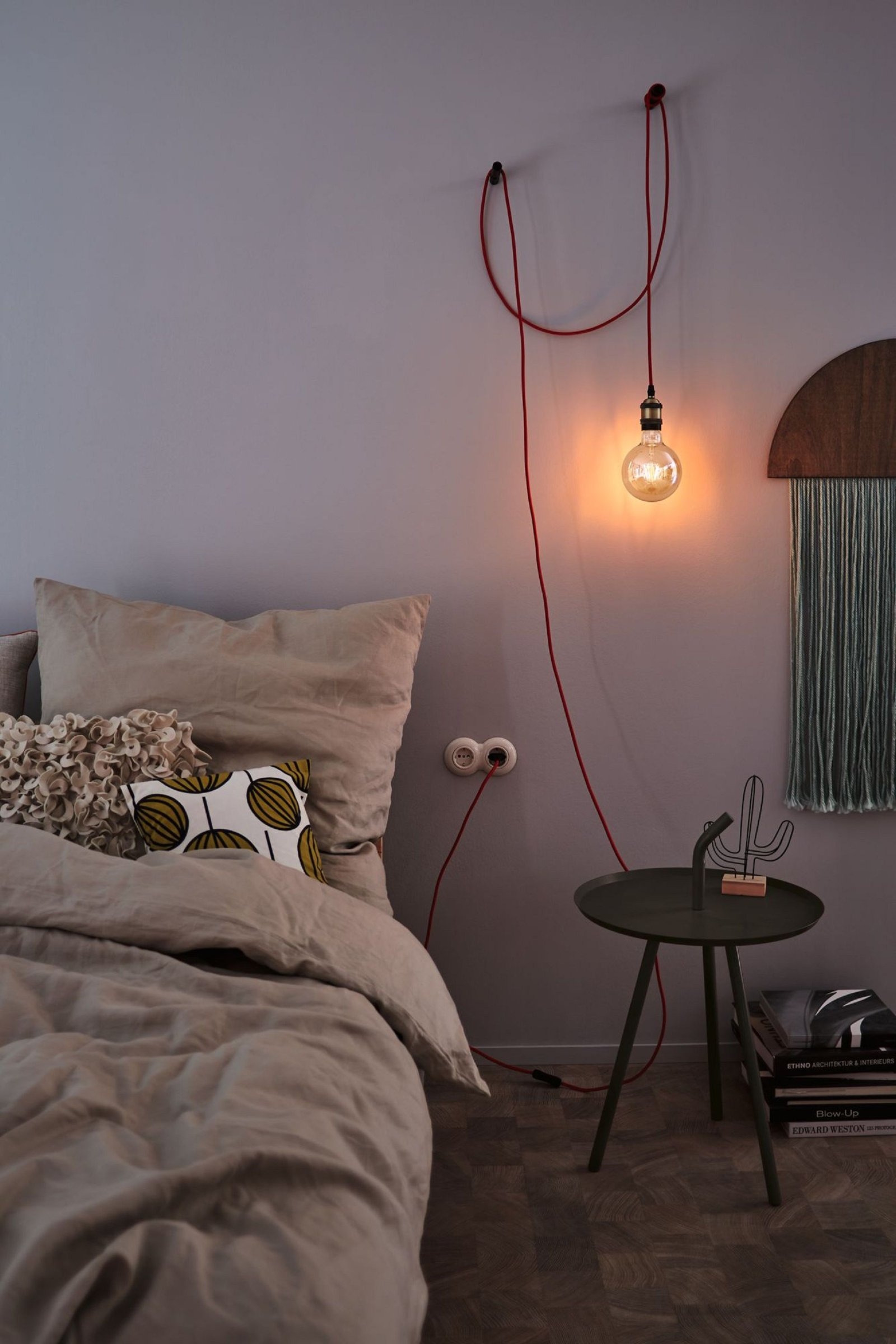 Escena de dormitorio con cama, lámpara colgante, mesa auxiliar y decoración mural.
