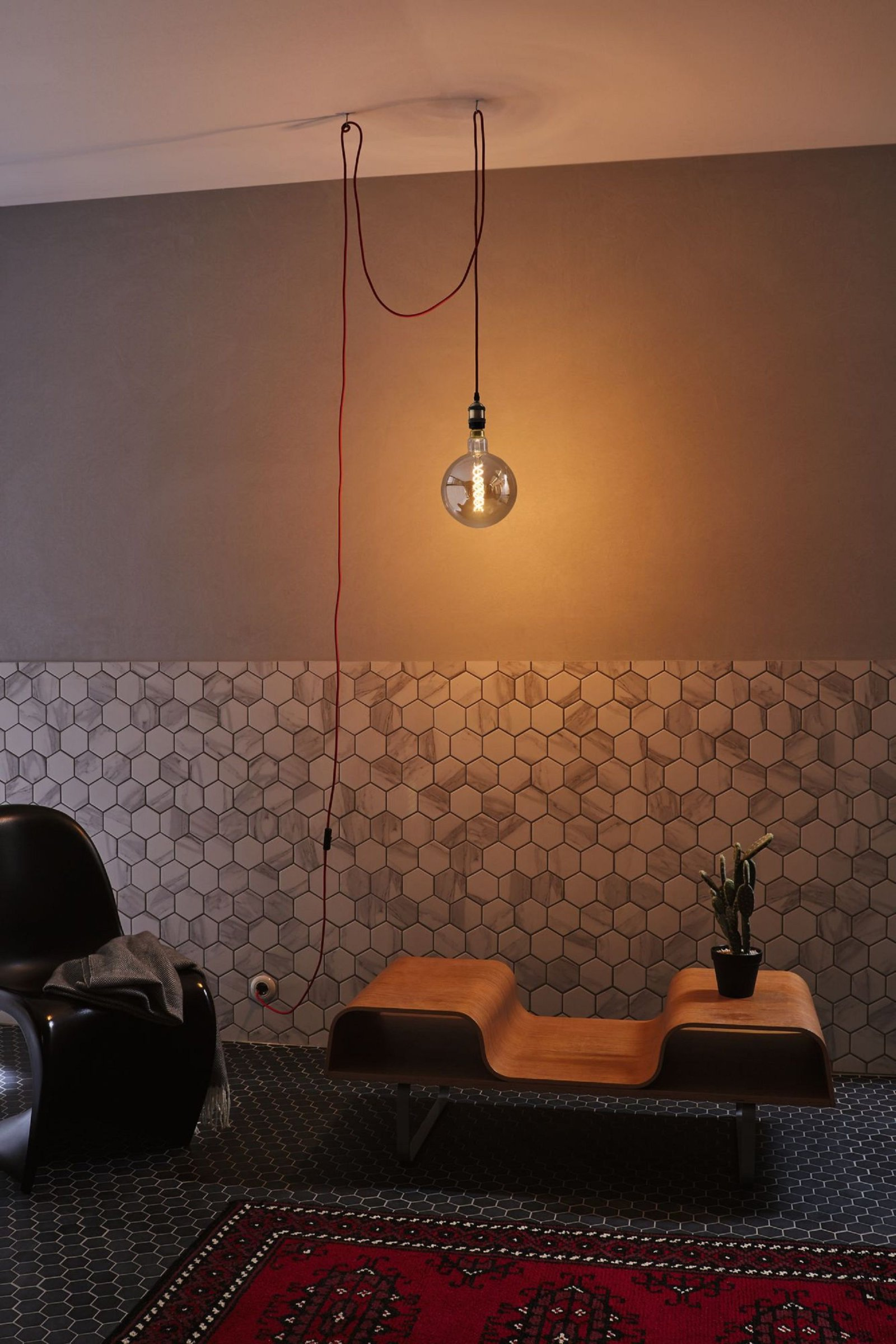 Una habitación con una lámpara colgante, un banco y una alfombra. Las paredes son de dos tonos.