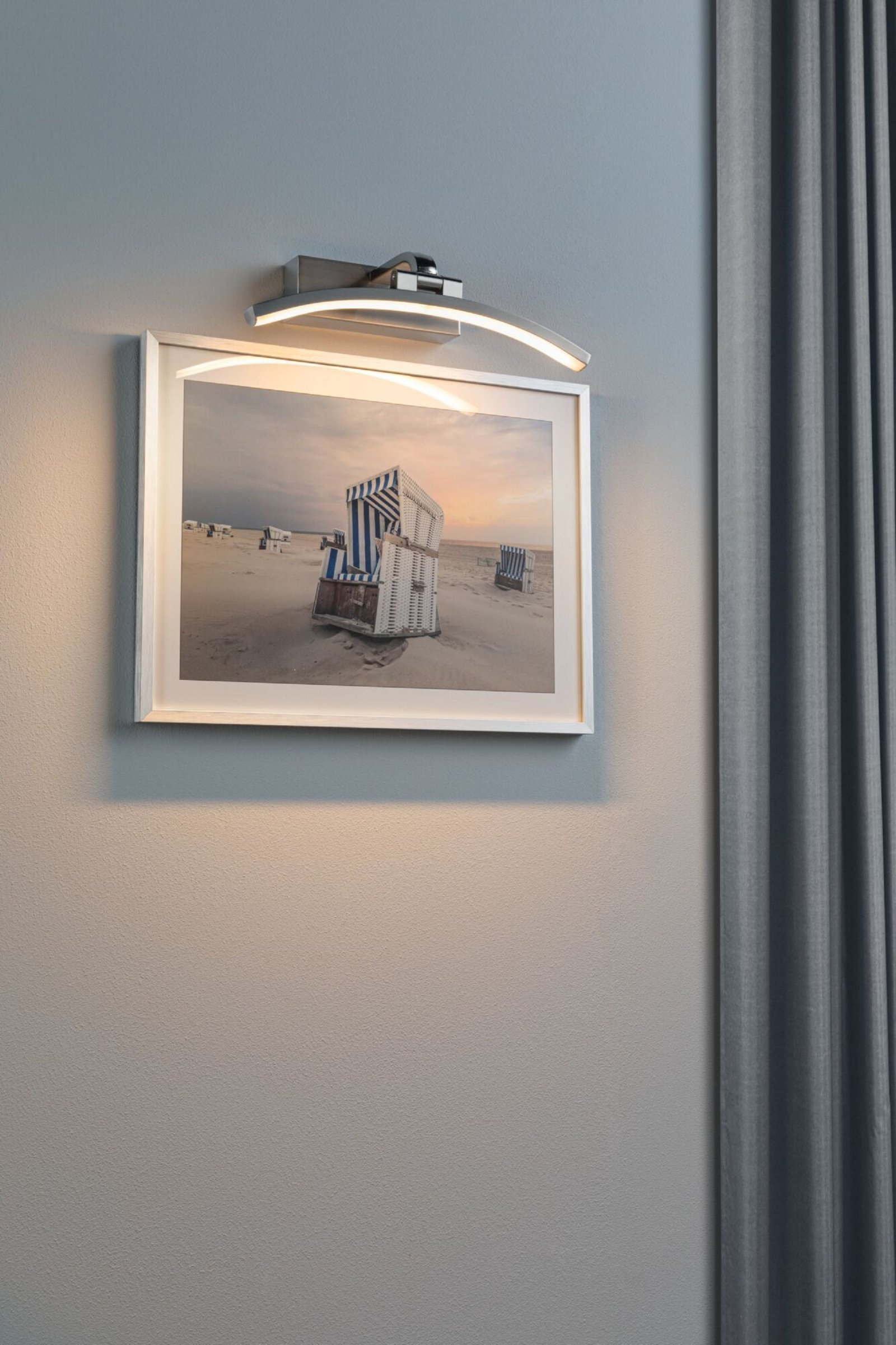 Obraz leżaków na ścianie z białą ramą, z lampą nad nim.