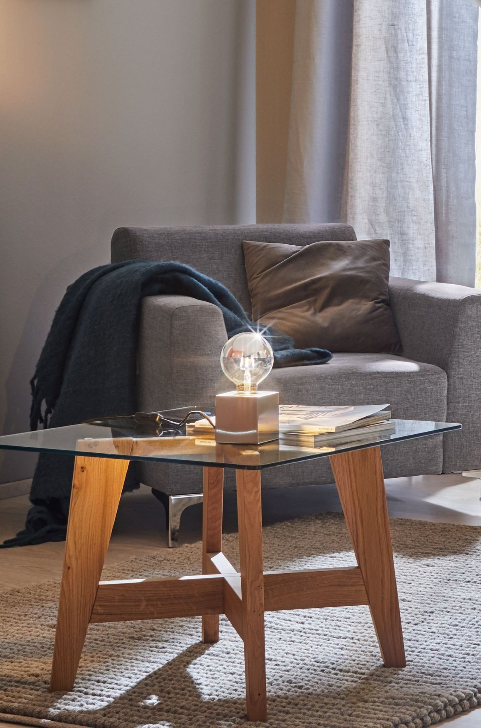 Szklany stolik kawowy z lampą i kanapą w tle. Przytulna atmosfera.